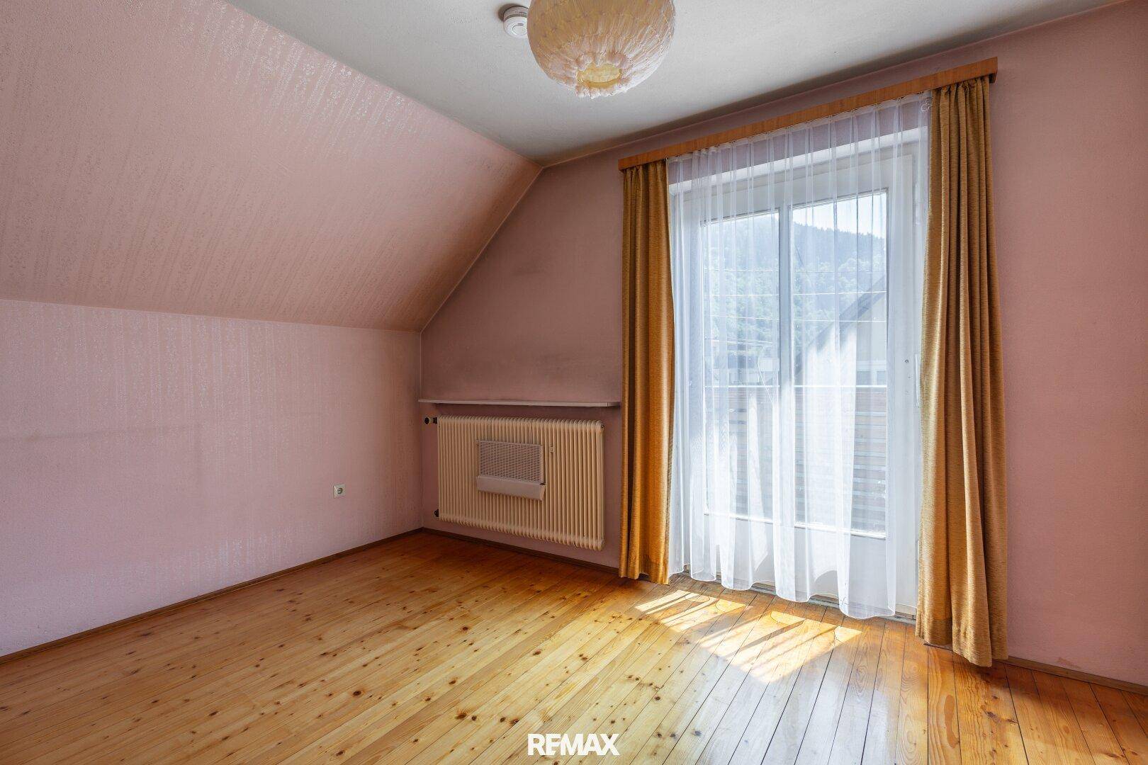 Schlafzimmer im Dachgeschoss mit Holzboden, Fenster und rosa Wänden.