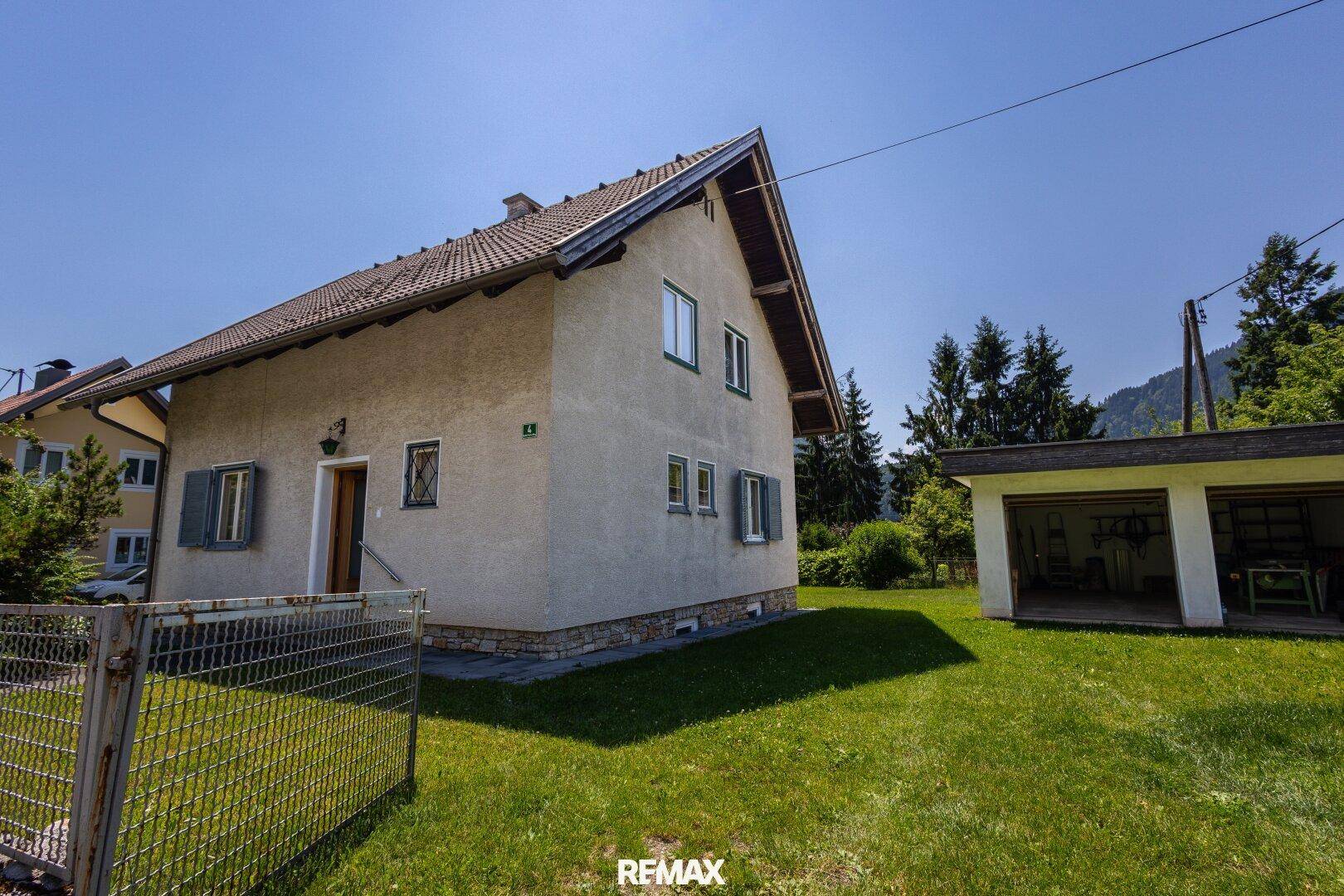 Seitenansicht des Hauses mit Garten, Zaun und separatem Garagengebäude.