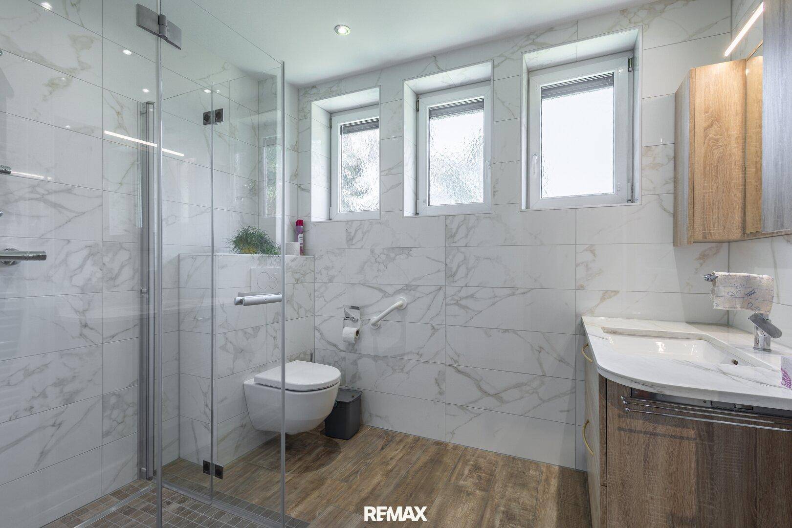 Modernisiertes Badezimmer mit großen Marmorfliesen, ebenerdiger Dusche und Fenster für Tageslicht.