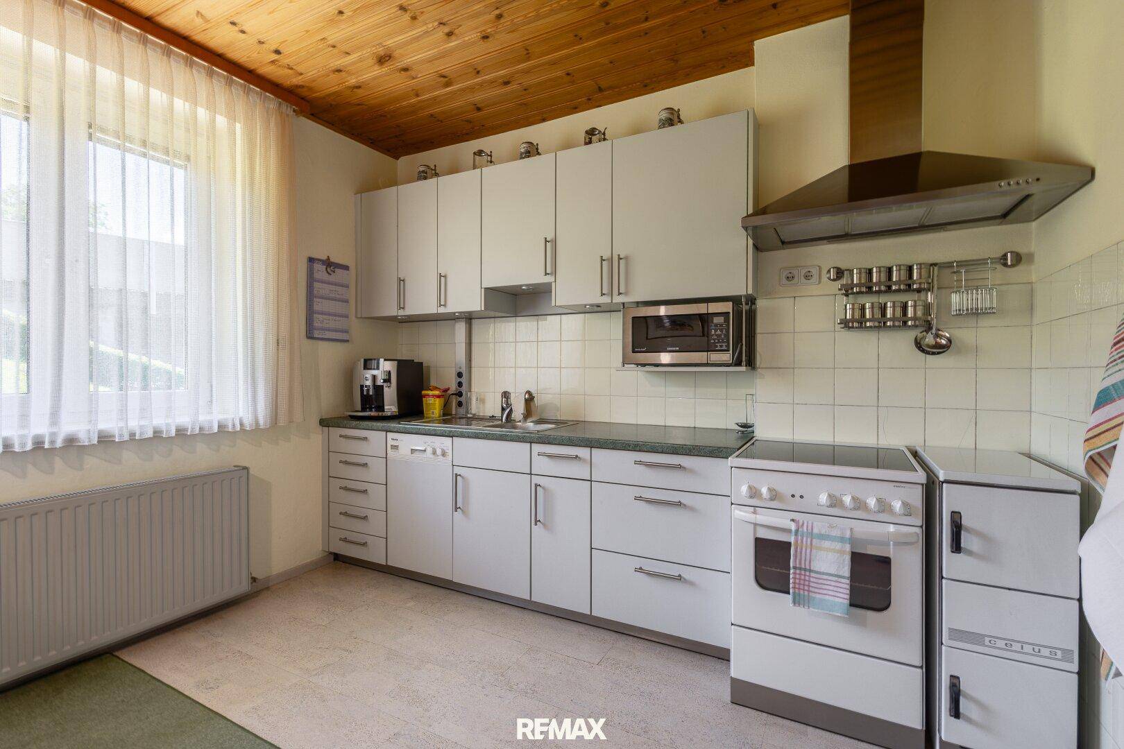 Funktionale Küche mit weißen Schränken, Fliesenrückwand und Holzdecke, bereit zur Modernisierung.