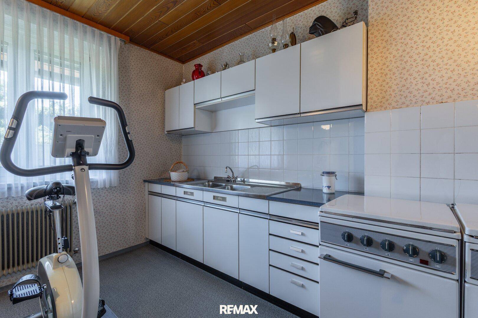 Kleine Küche oder Hauswirtschaftsraum mit weißen Schränken, Fliesenrückwand und Trainingsgerät.