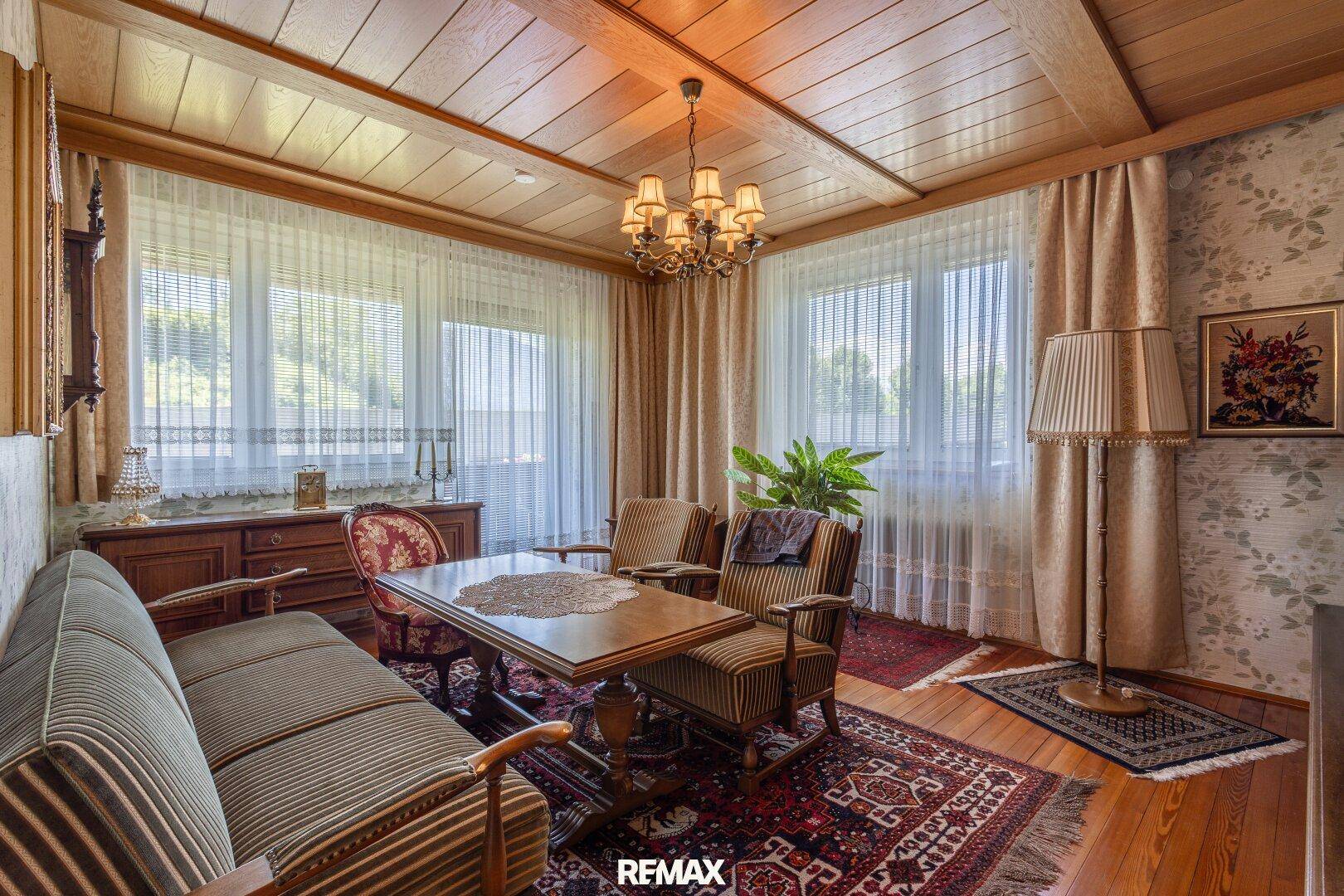 Traditionell eingerichtetes Wohnzimmer mit Holzbalkendecke, Teppich und großen Fenstern.