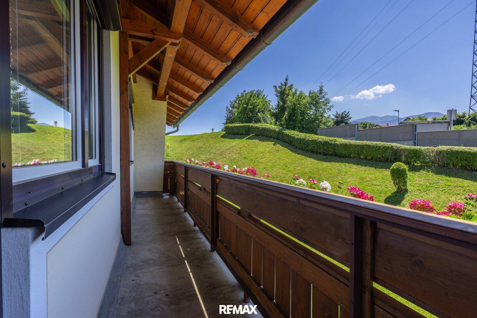 Langer Holzbalkon mit Blumenkästen und Blick auf die grüne Hügellandschaft.
