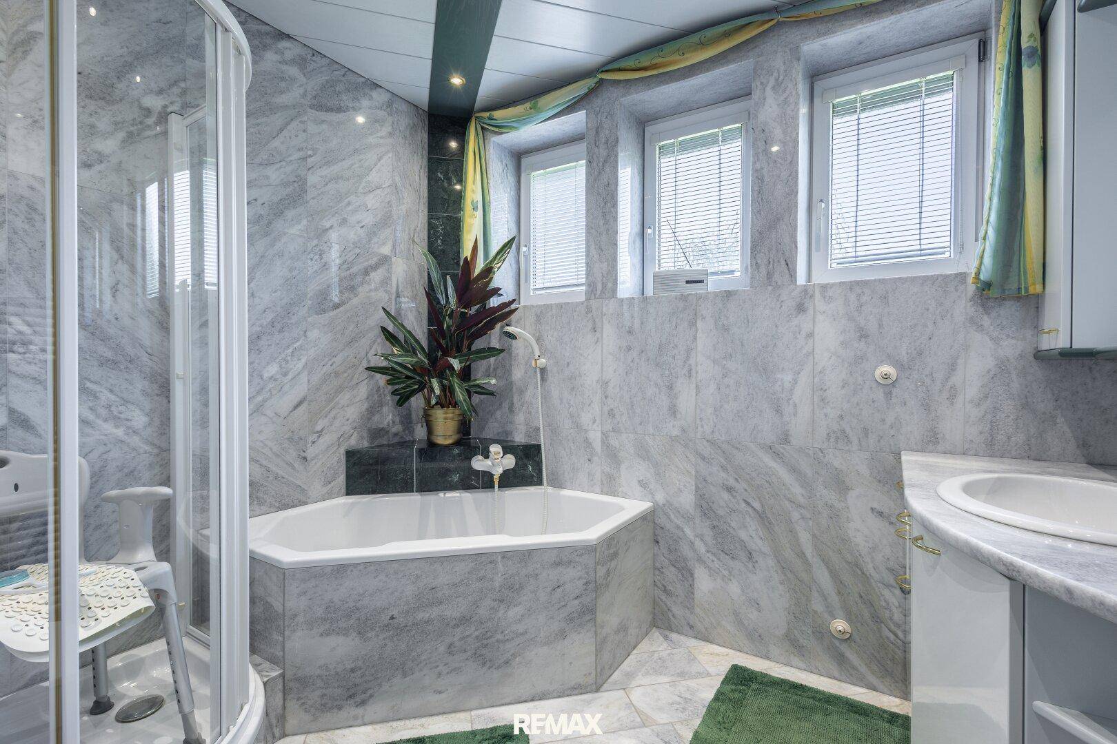 Badezimmer mit Marmorfliesen, Eckbadewanne, Dusche und mehreren Fenstern.