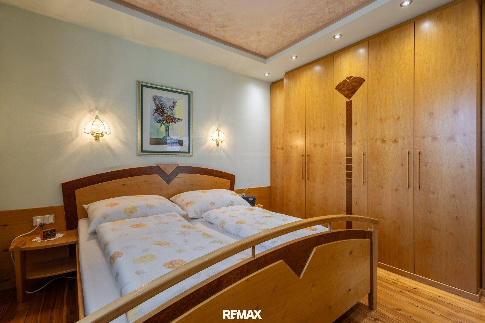 Helles Schlafzimmer mit Einbauschränken, Holzboden und indirekter Deckenbeleuchtung.