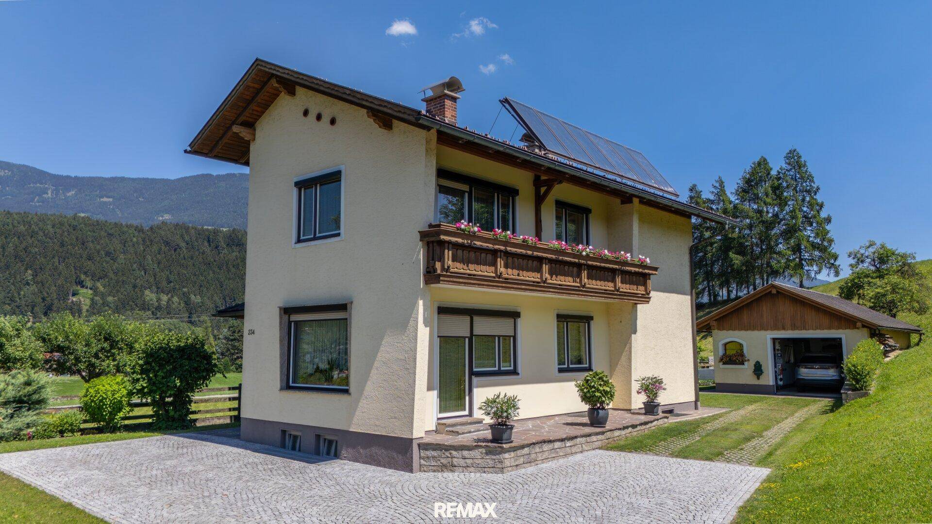 Freistehendes Einfamilienhaus mit gepflasterter Auffahrt, Balkon und Solaranlage auf dem Dach.