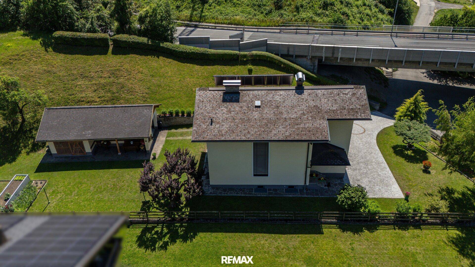 Luftaufnahme des Hauses mit Satteldach, großem Garten und gepflasterter Zufahrt, nahe einer Brücke.