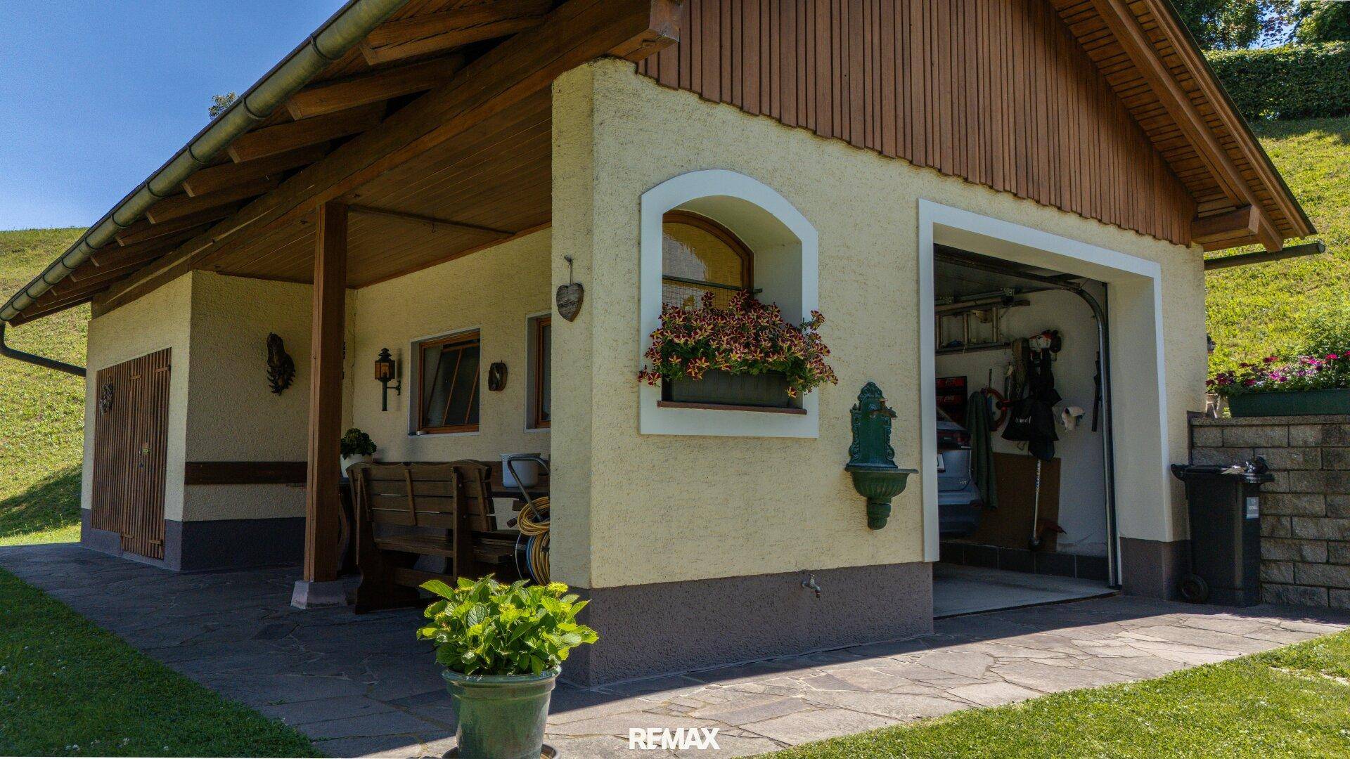 Nebengebäude mit Garage, überdachtem Sitzbereich und Blumenkästen.