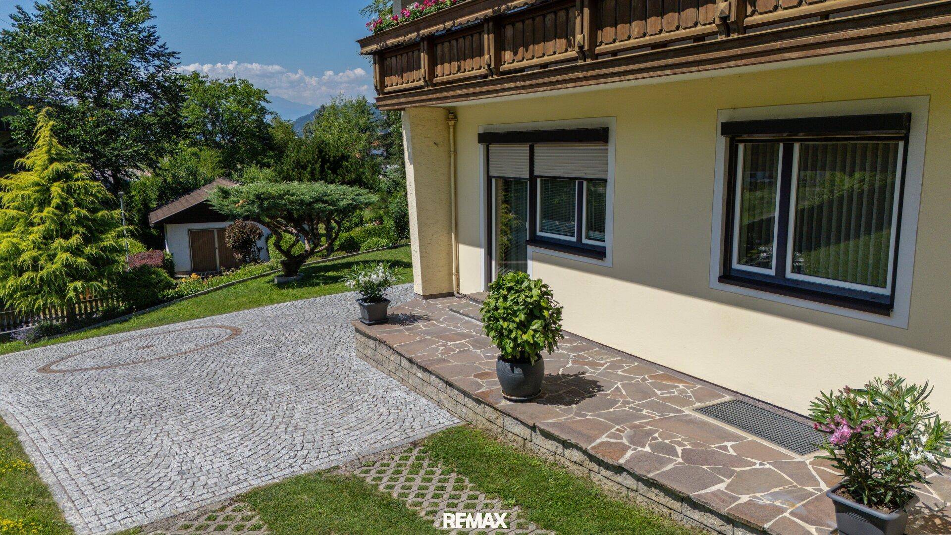 Seitlicher Eingangsbereich des Hauses mit gepflasterter Terrasse und Blick auf die grüne Umgebung.