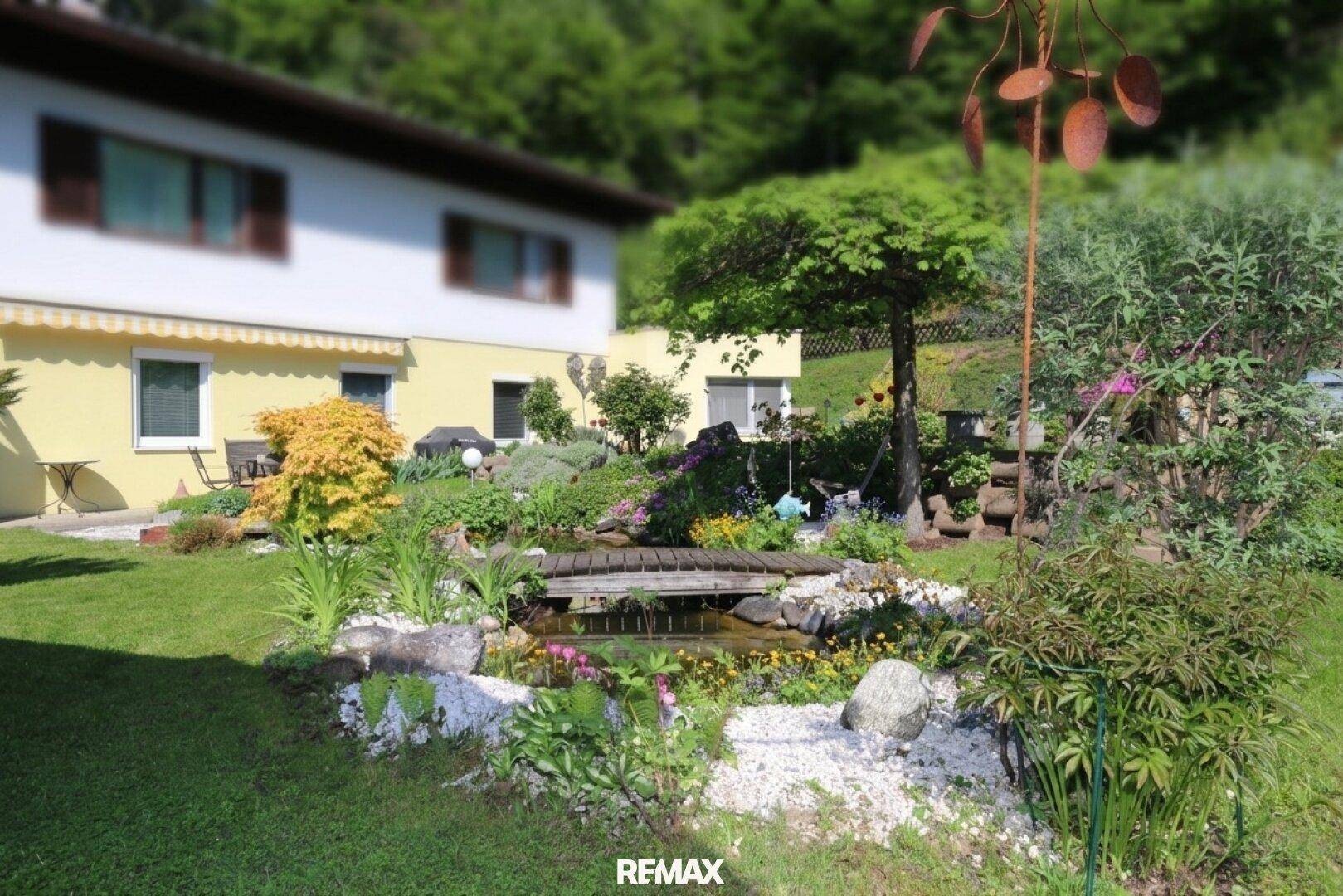 Malerischer Garten mit Teich, üppiger Vegetation und Blick auf das Wohnhaus.
