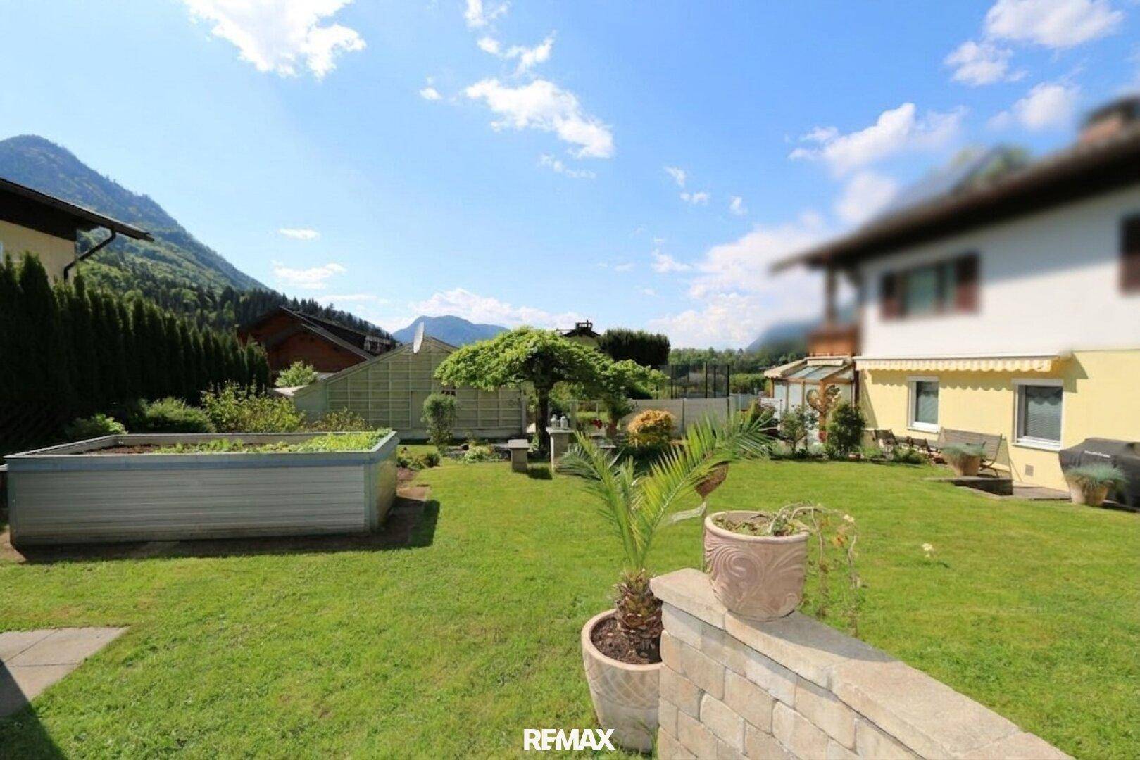 Sonniger Garten mit Rasenfläche, Palmen und beeindruckendem Bergblick im Hintergrund.