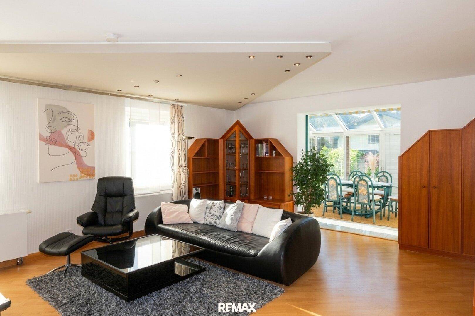 Großzügiges Wohnzimmer mit Ledersofa, Holzboden und offenem Zugang zum Wintergarten.