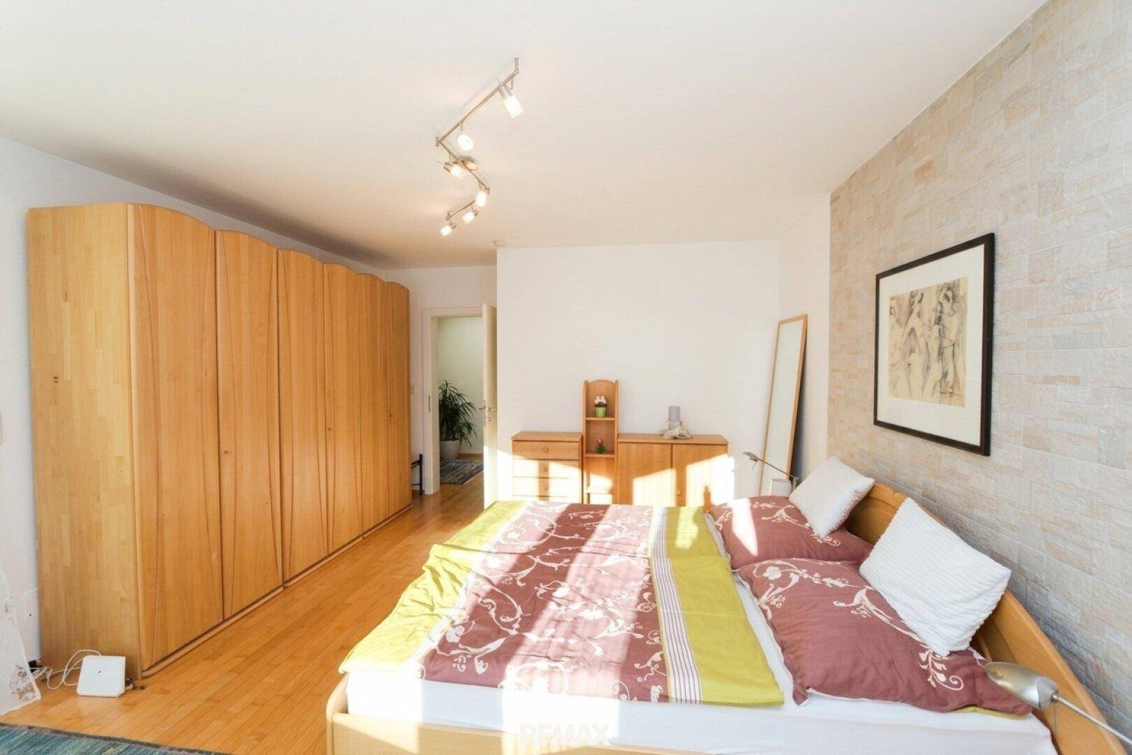 Helles Schlafzimmer mit großem Holzschrank, Holzboden und viel Tageslicht.