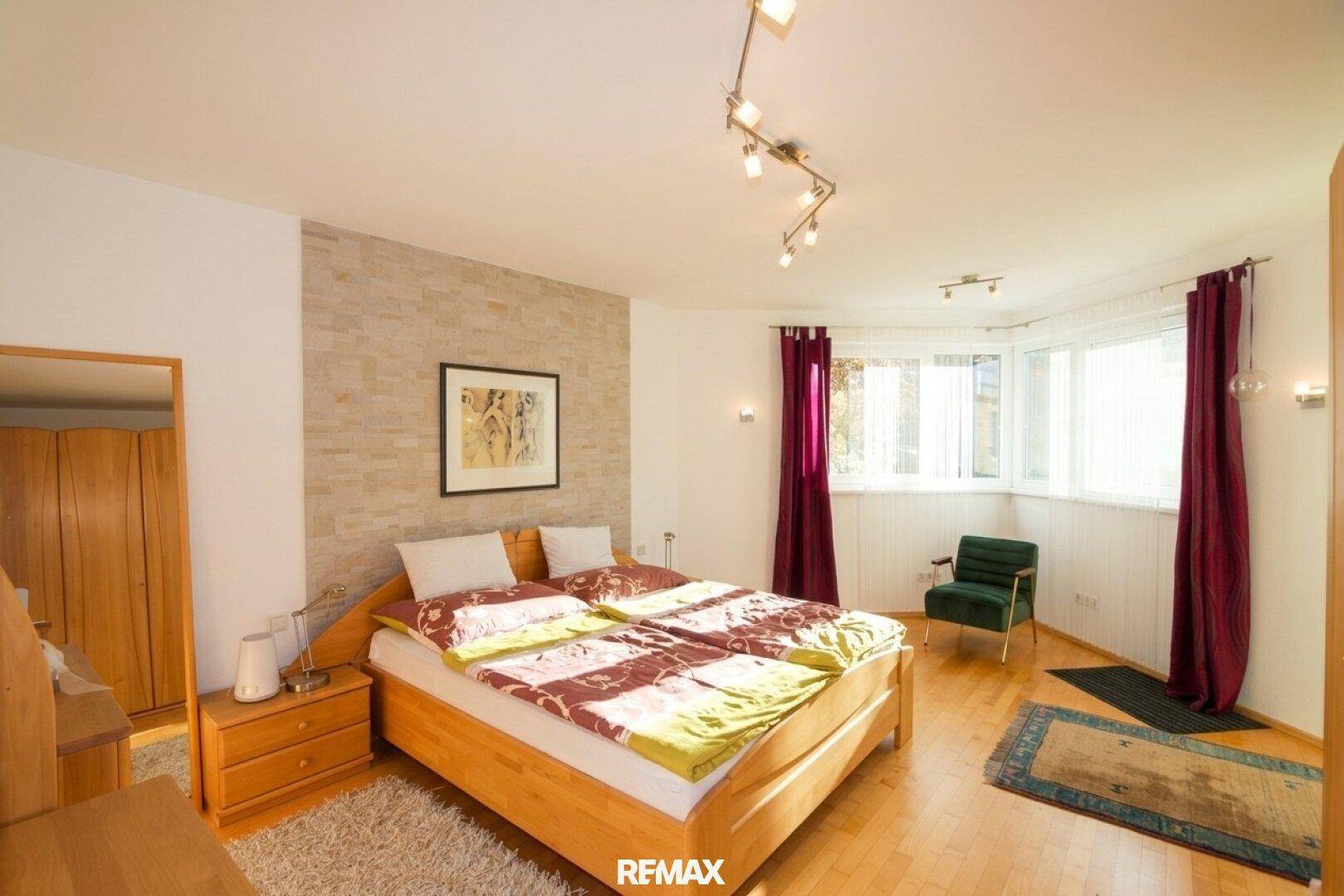 Gemütliches Schlafzimmer mit Holzboden, einer Akzentwand aus Stein und großen Fenstern für viel Licht.