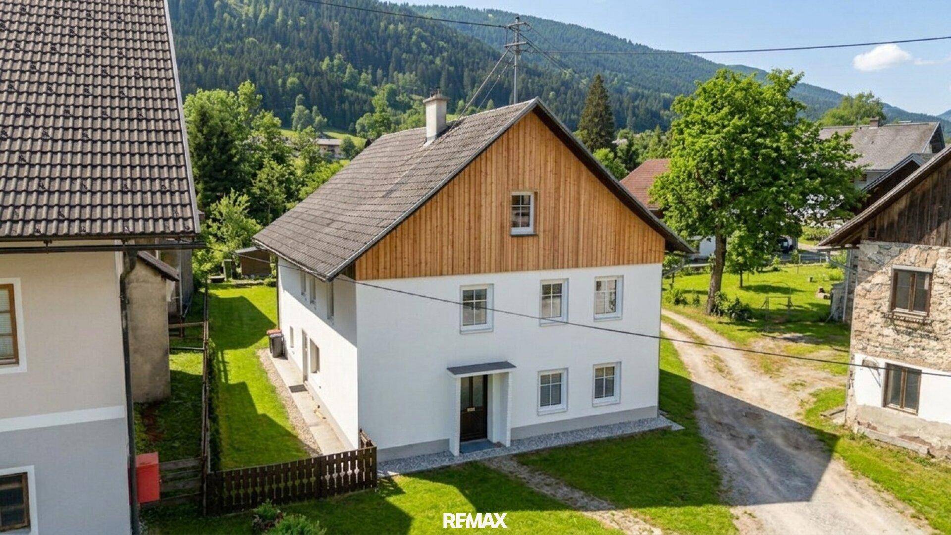 Haus mit traditioneller Architektur, weißer Fassade und Holzverkleidung, umgeben von ländlicher Idylle.
