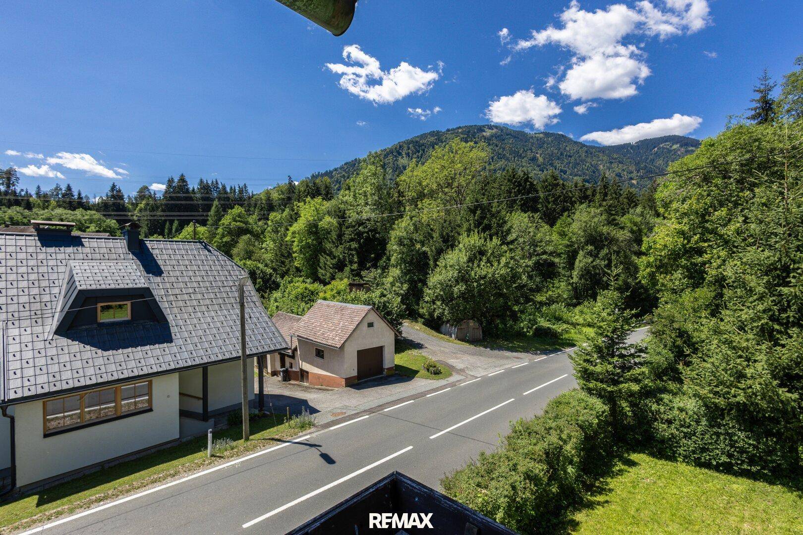 Haus in ländlicher Umgebung mit Bergblick und angrenzender Straße.