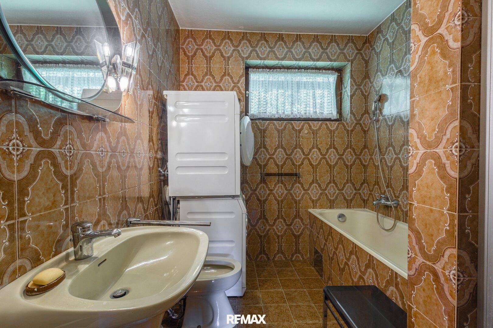 Badezimmer mit braunen Fliesen, Badewanne und Fenster.