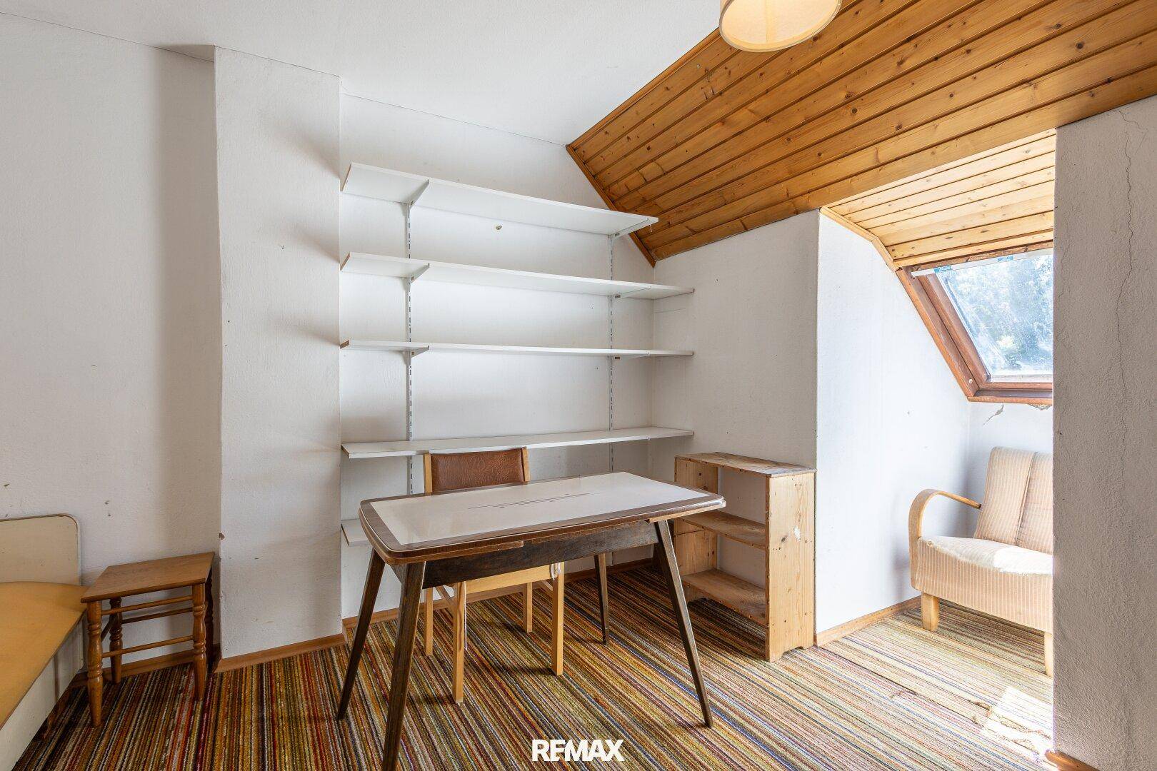Dachzimmer mit Holzdecke, Dachfenster und einfacher Einrichtung.