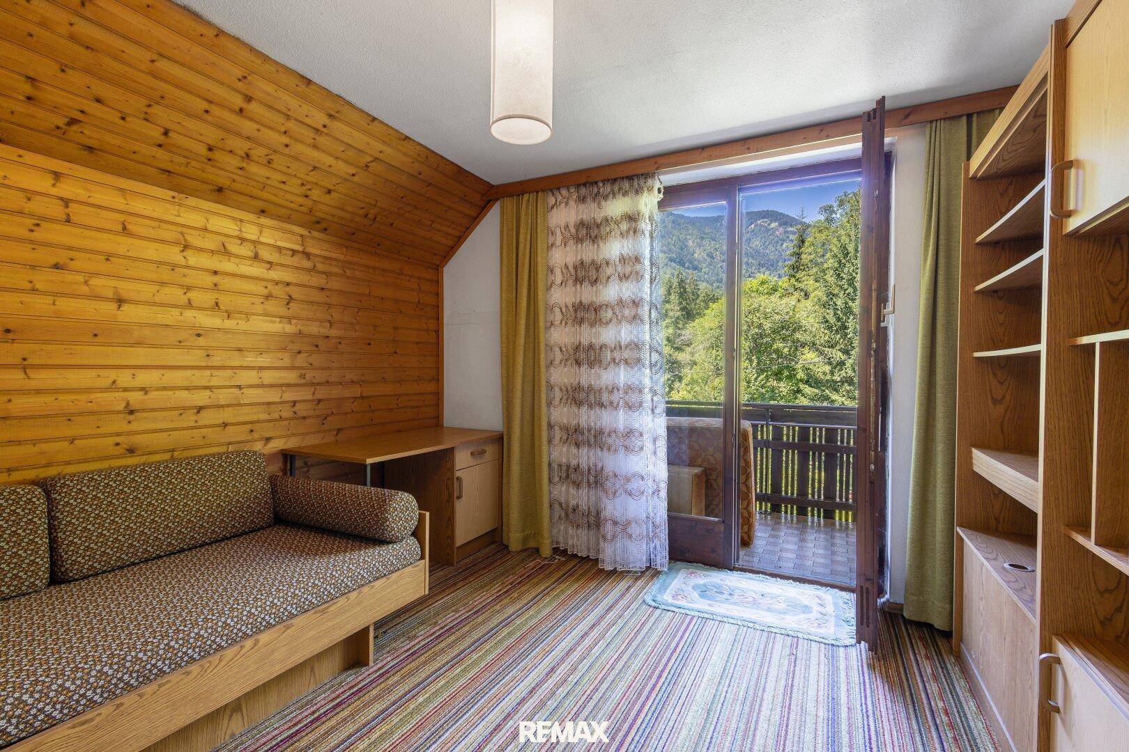 Gemütliches Dachzimmer mit Holzverkleidung, Balkonzugang und Bergblick.