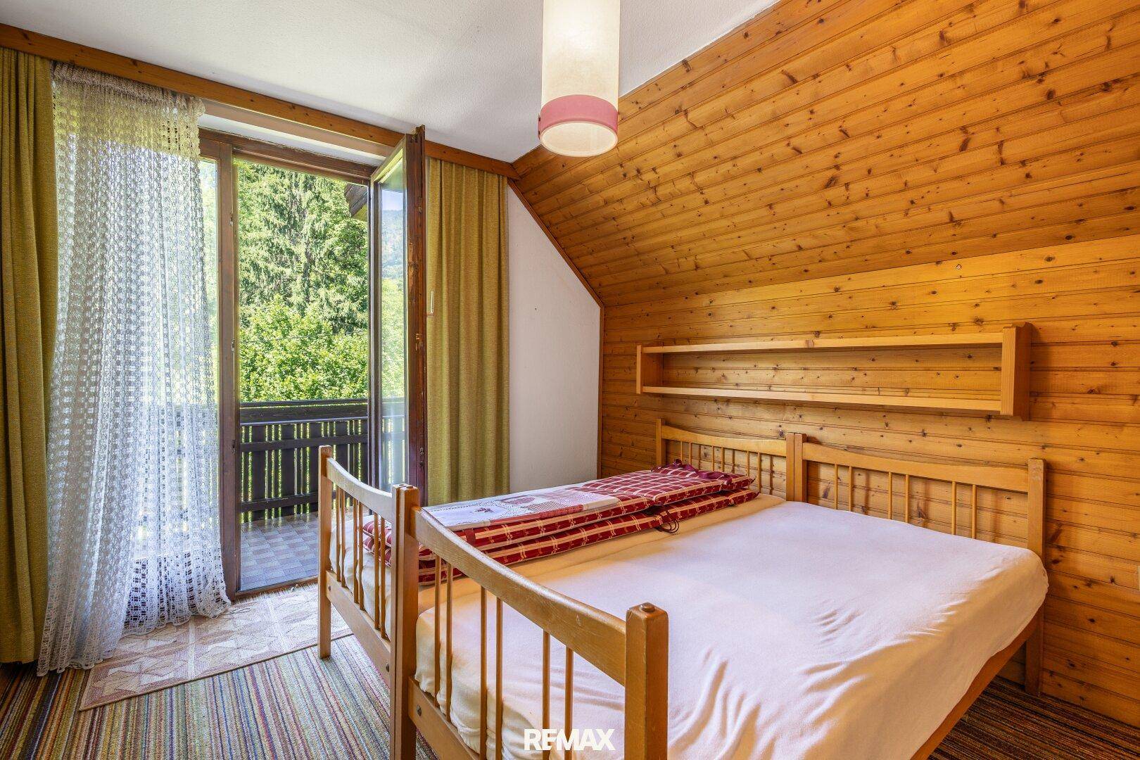 Schlafzimmer im Dachgeschoss mit Holzverkleidung, Doppelbett und Balkonzugang.