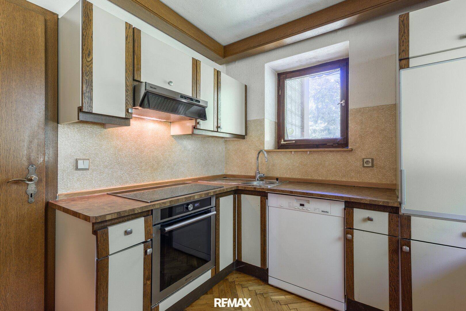 Funktionale Küche mit Einbaugeräten, Holzfronten und Fensterblick.
