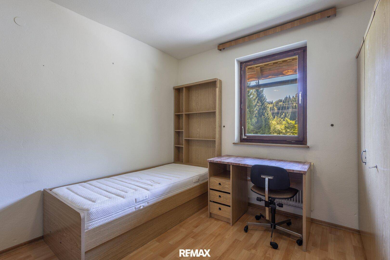 Einfaches Schlafzimmer mit Einzelbett, Schreibtisch und Blick ins Grüne.