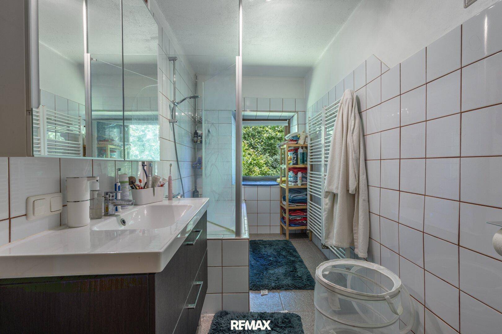 Modern gefliestes Badezimmer mit Duschkabine, Einzelwaschbecken, beheiztem Handtuchhalter und Fenster.