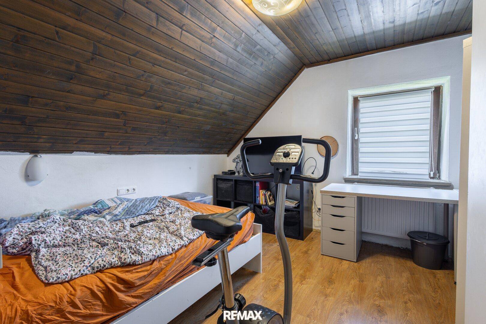 Gemütliches Schlafzimmer im Dachgeschoss mit dunkler Holzbalkendecke, Laminatboden und Bett.