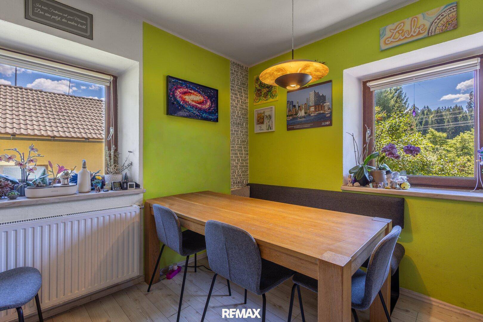 Heller Essbereich in der Küche mit Holztisch und grüner Akzentwand.