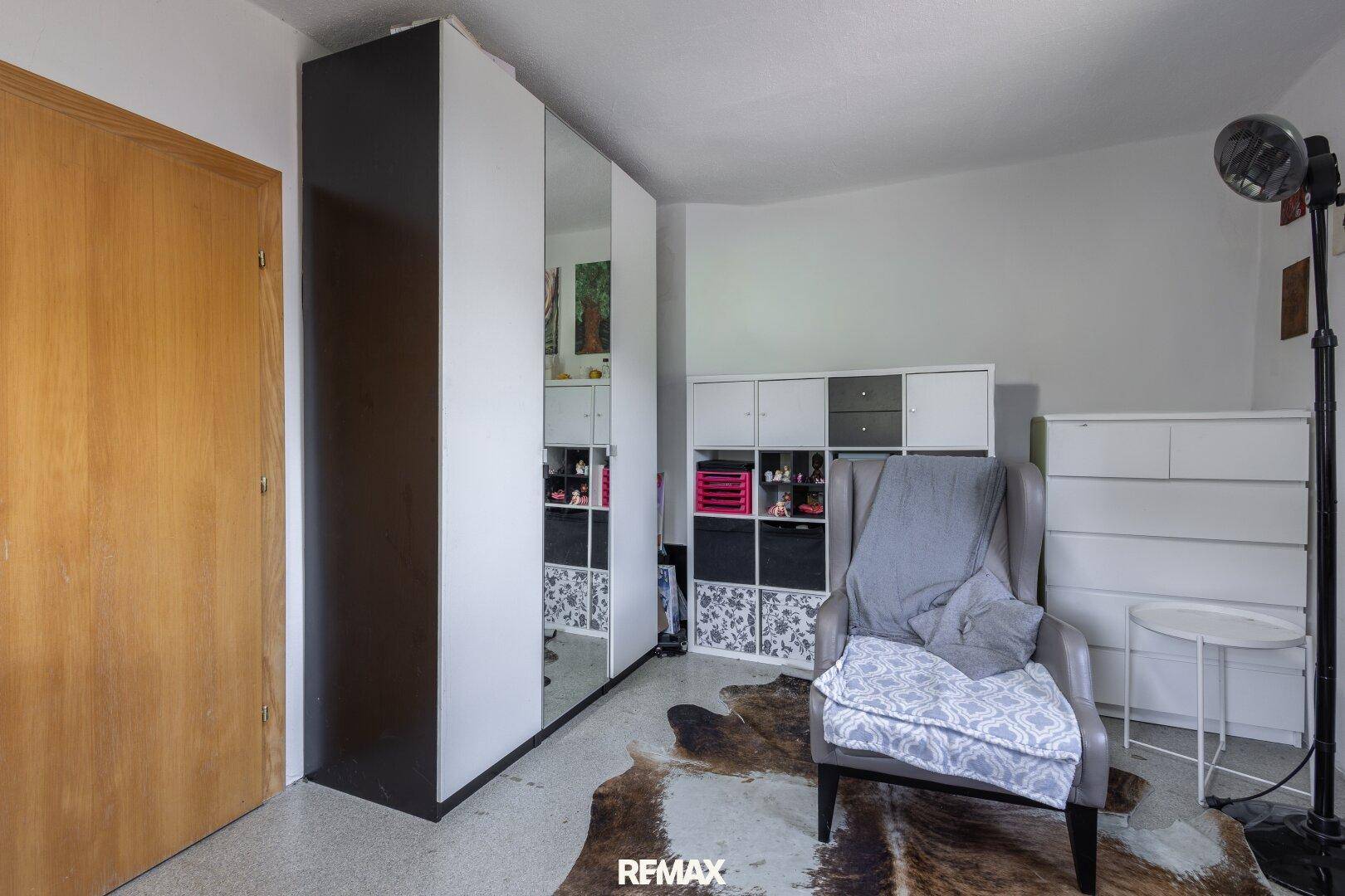Helles Zimmer mit großem Spiegelschrank, Sessel und Teppich in Felloptik, ideal als Ankleidezimmer.