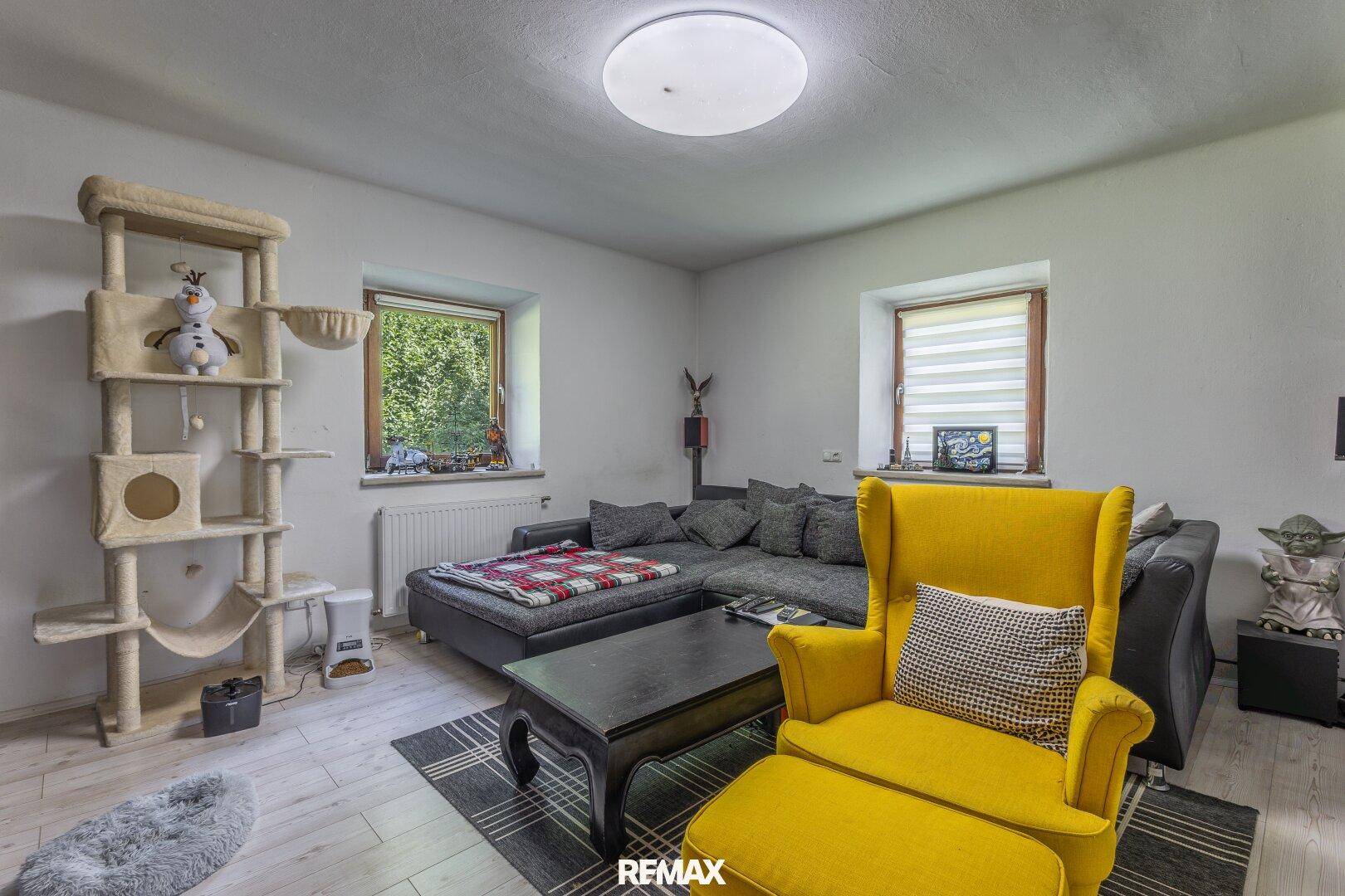 Modernes Wohnzimmer mit großem Sofa, Sessel und Blick ins Grüne.