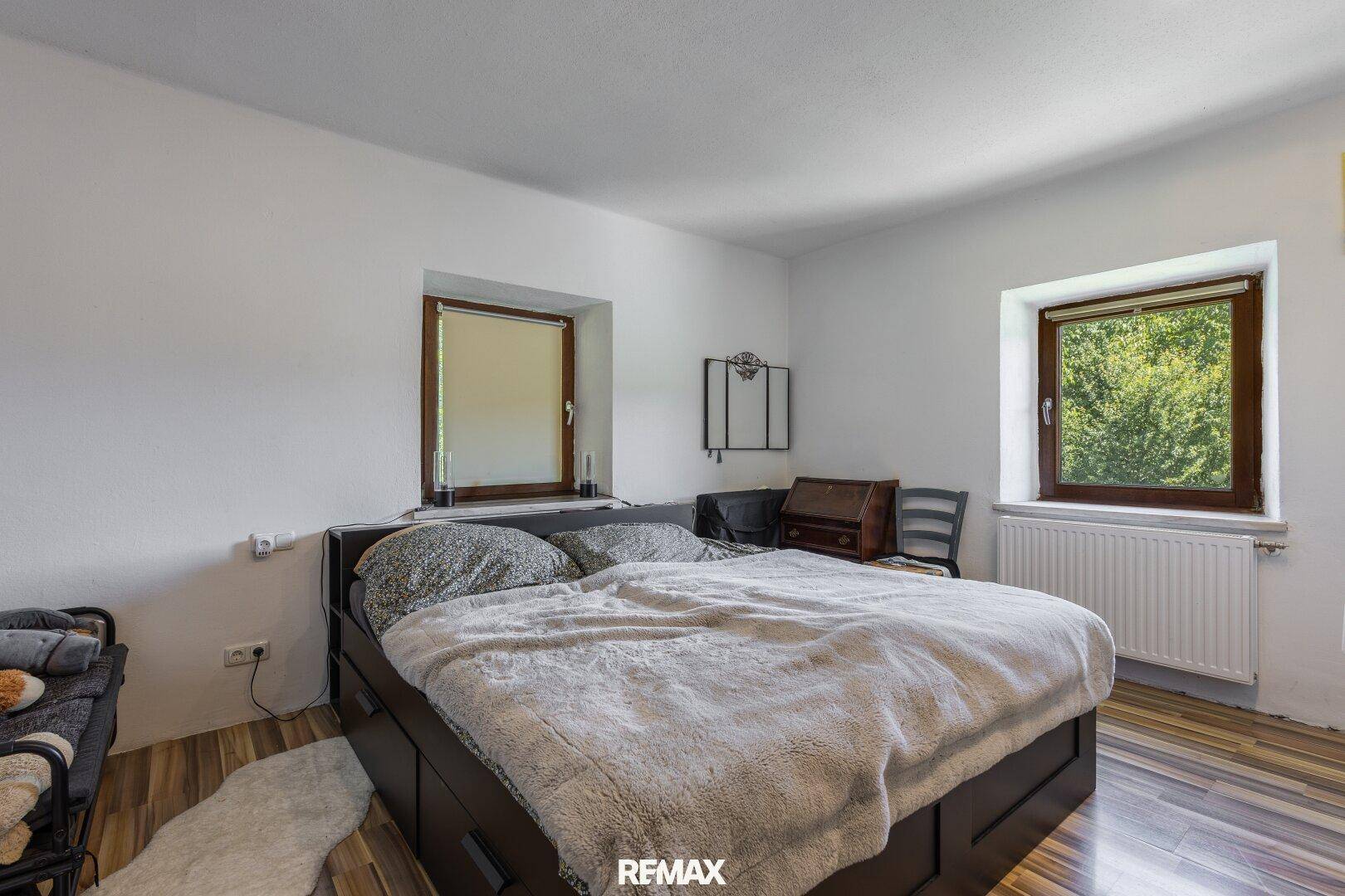 Gemütliches Schlafzimmer mit Holzboden, Doppelbett und zwei Fenstern mit Blick ins Grüne.
