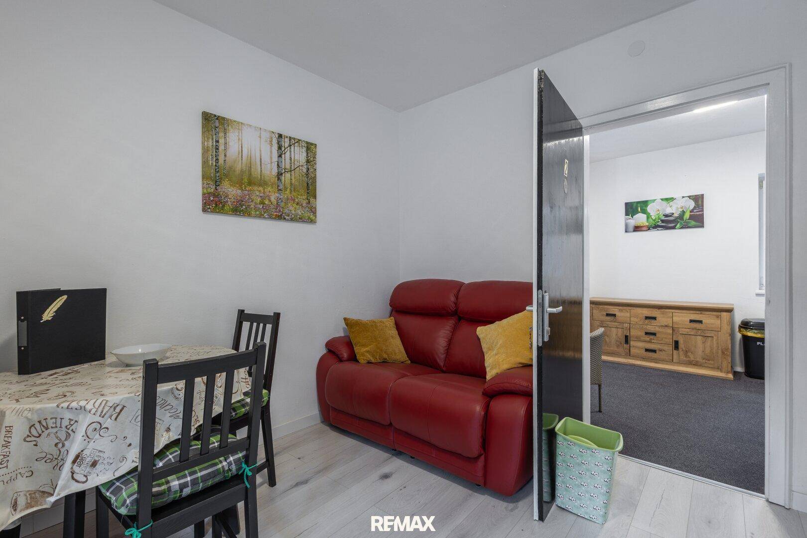 Essbereich mit Tisch und rotem Sofa, angrenzend an einen weiteren Raum mit Holzmöbeln.