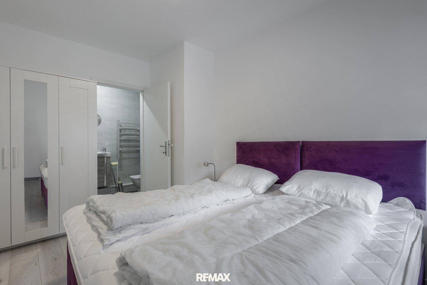 Schlafzimmer mit Doppelbett und Kleiderschrank, mit direktem Zugang zu einem Badezimmer.
