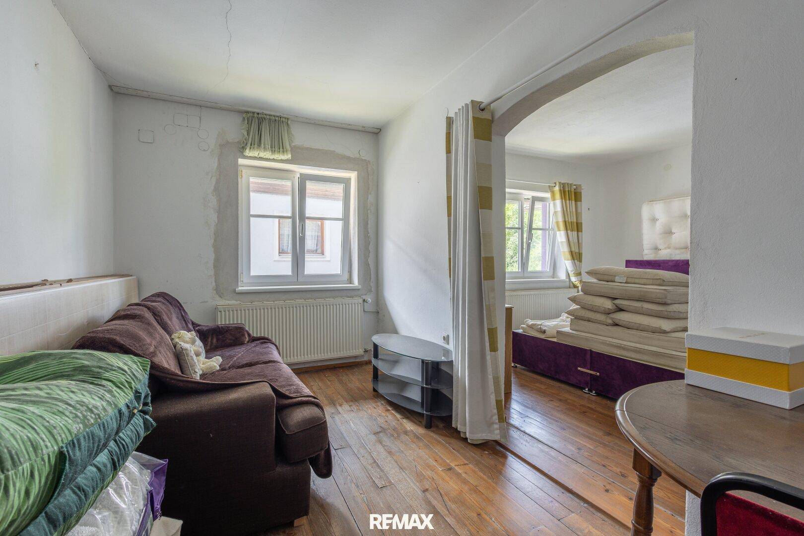 Wohnbereich mit Sofa und Holzboden, der zu einem Schlafbereich mit Bett führt.