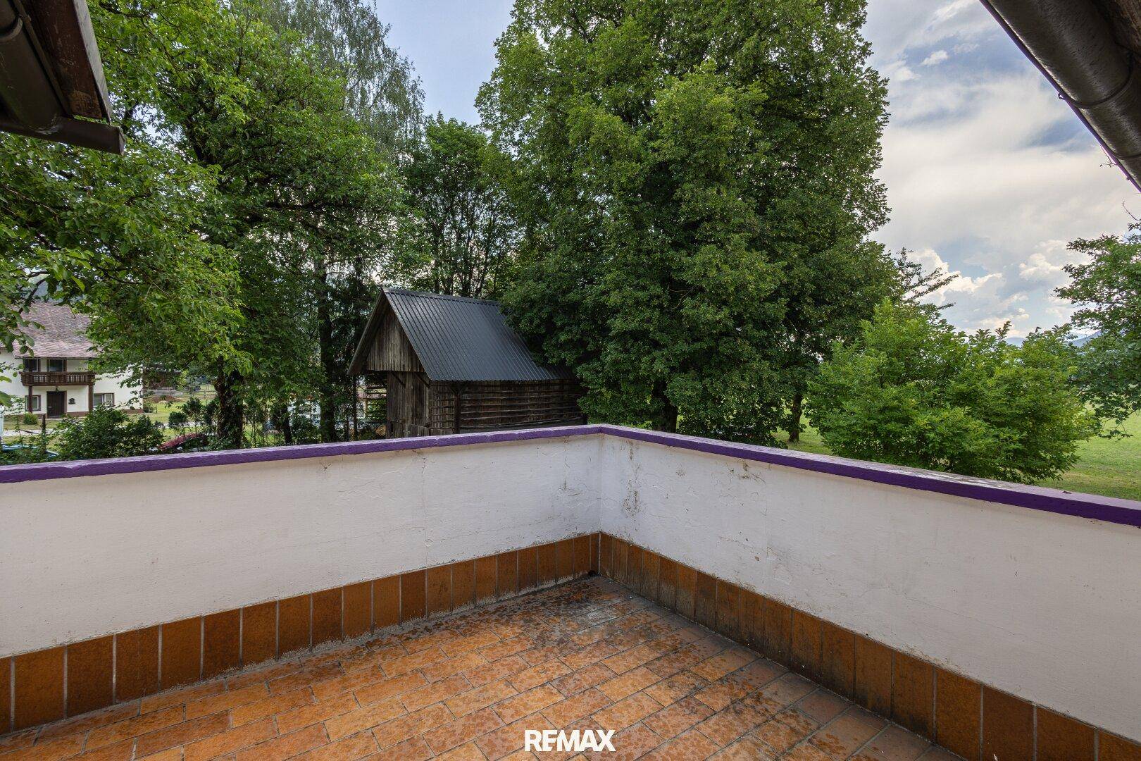 Balkon mit Fliesenboden und Blick auf grüne Bäume und die umliegende Natur.