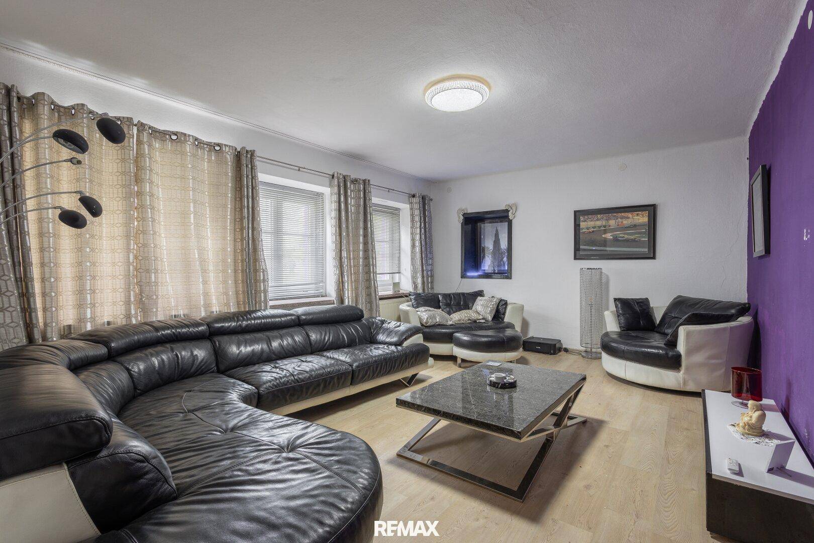 Geräumiges Wohnzimmer mit großer Ledercouch, Couchtisch und lila Akzentwand.