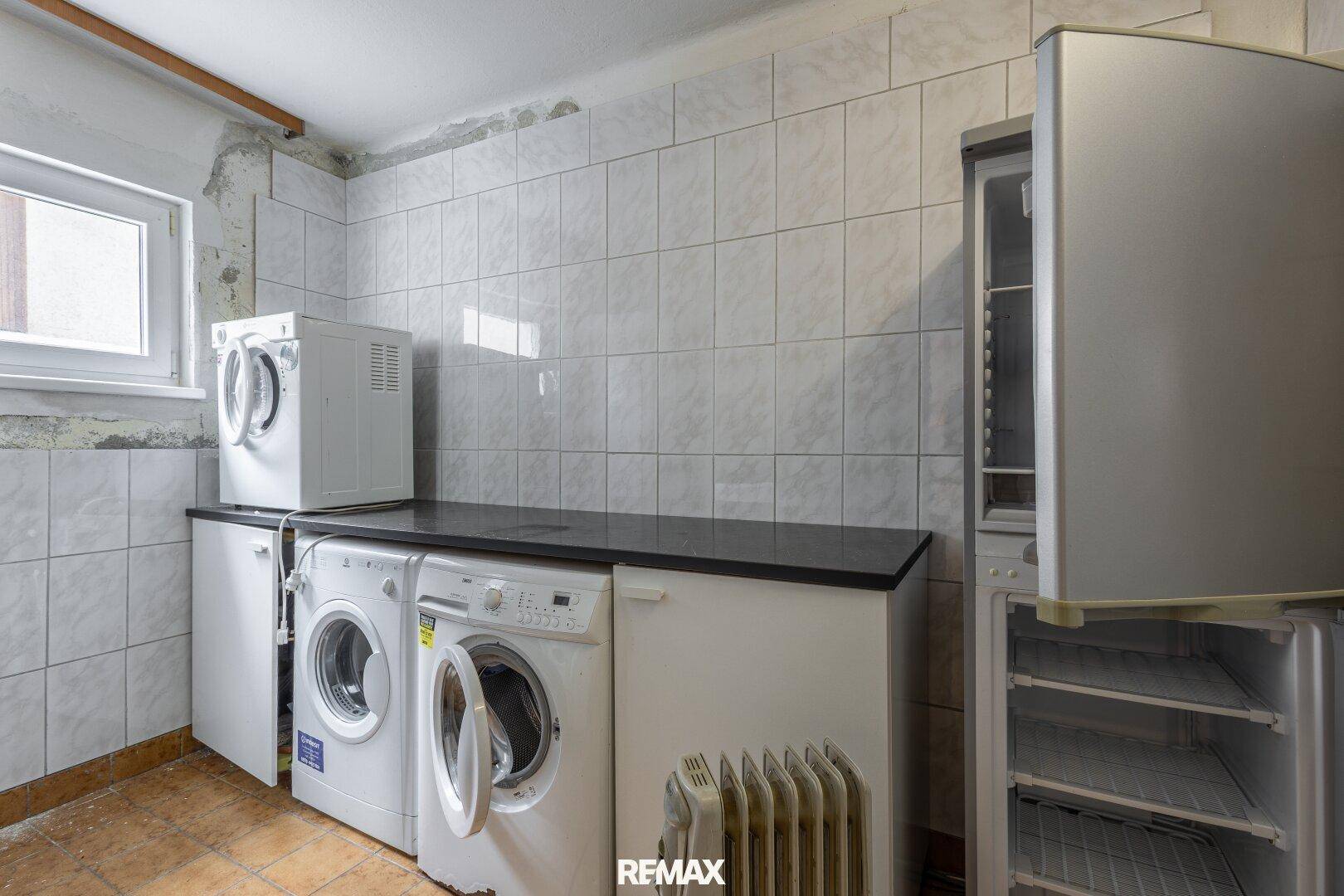 Hauswirtschaftsraum mit Waschmaschinen, Trockner und Kühlschrank, gefliesten Wänden und Fenster.