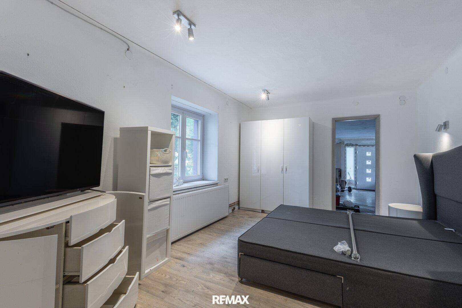 Helles Schlafzimmer mit großem Bett, Kleiderschrank und Fernseher, ausgestattet mit Laminatboden.