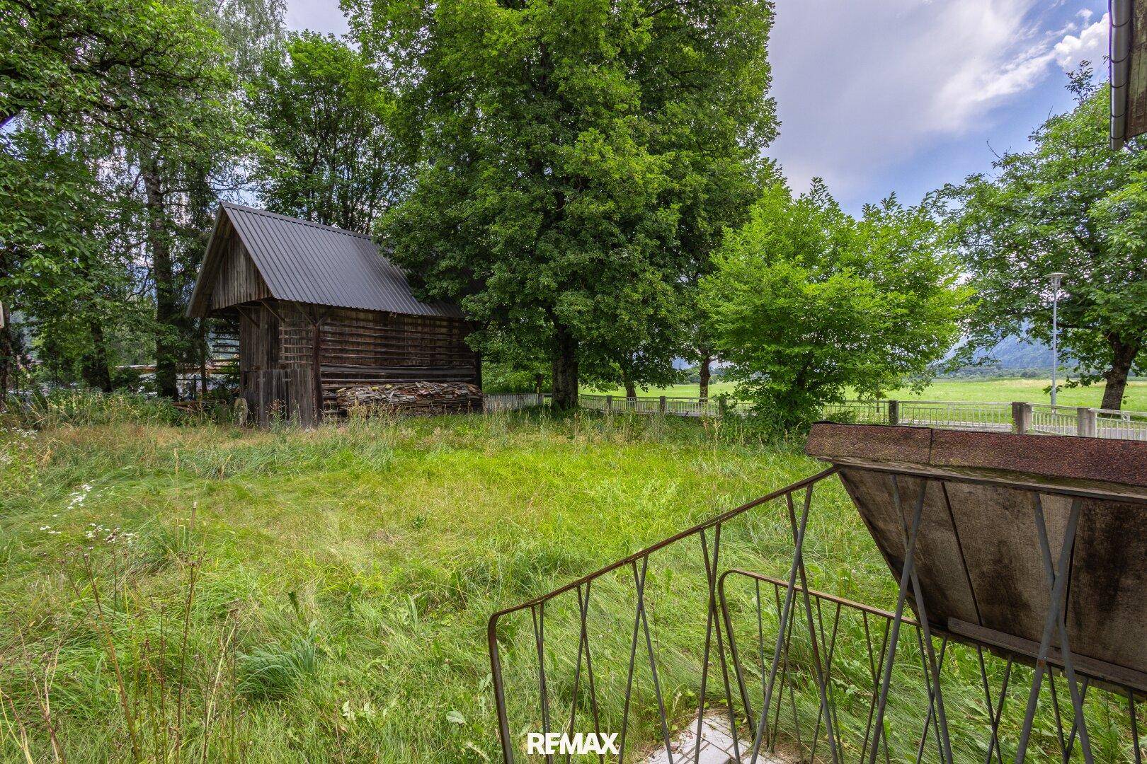 Rustikaler Holzschuppen in einem verwilderten Garten mit Blick auf die Berge.