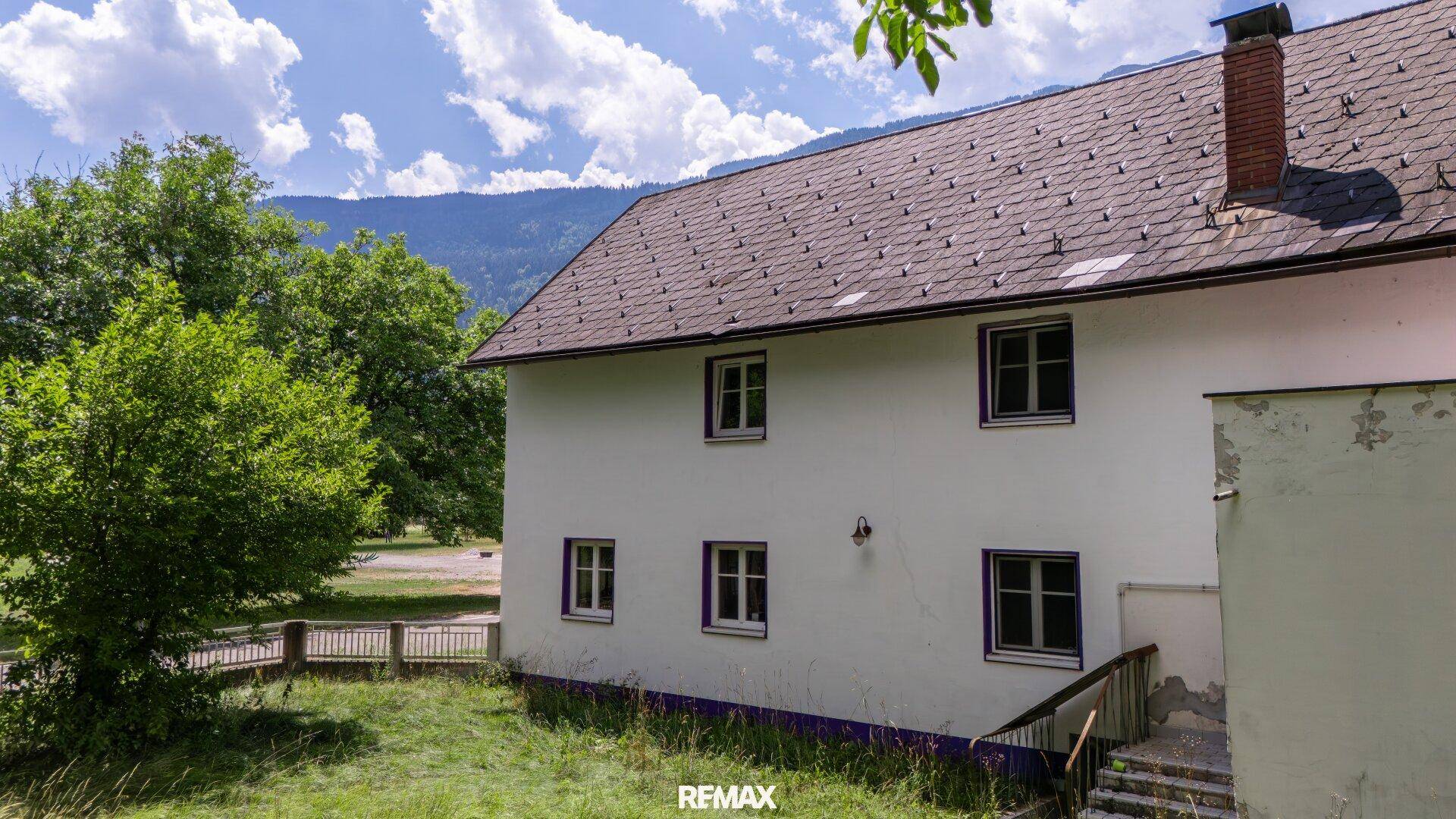 Seitenansicht eines weißen Hauses mit Satteldach und Bergblick.