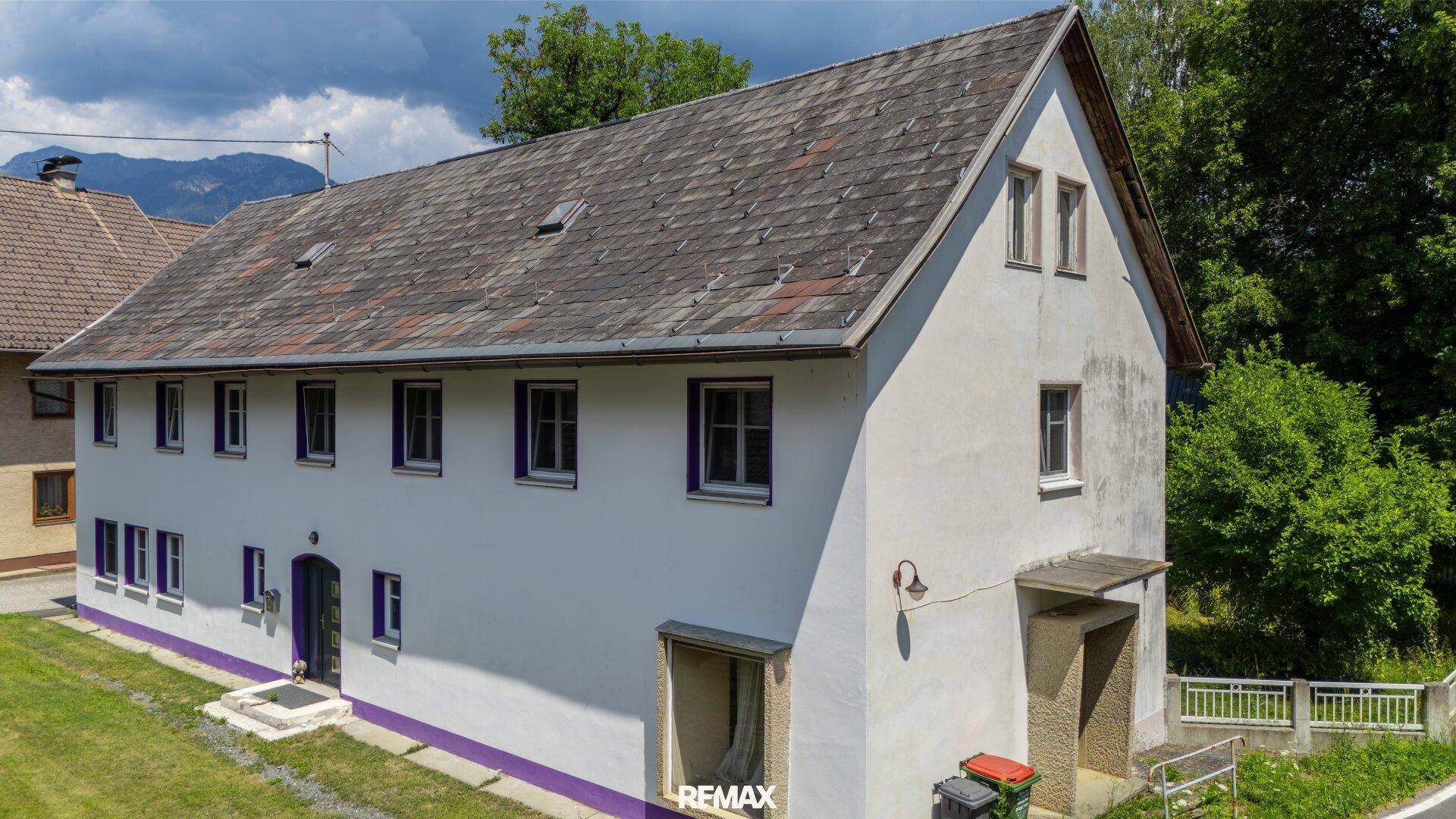 Vorderansicht des weißen Hauses mit dunklem Dach und ländlicher Umgebung.