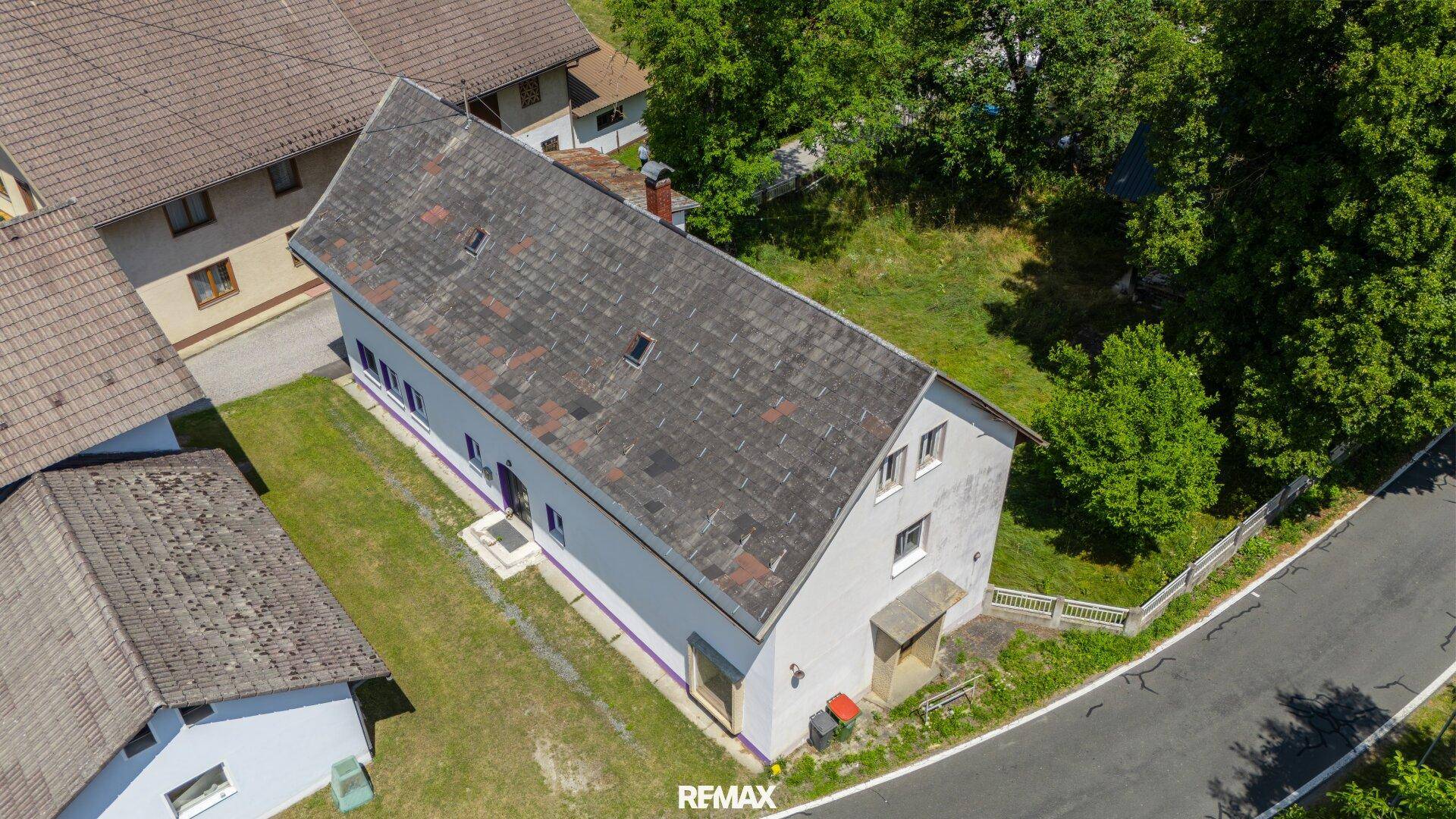 Vogelperspektive des langen weißen Hauses mit Satteldach und angrenzender Straße.
