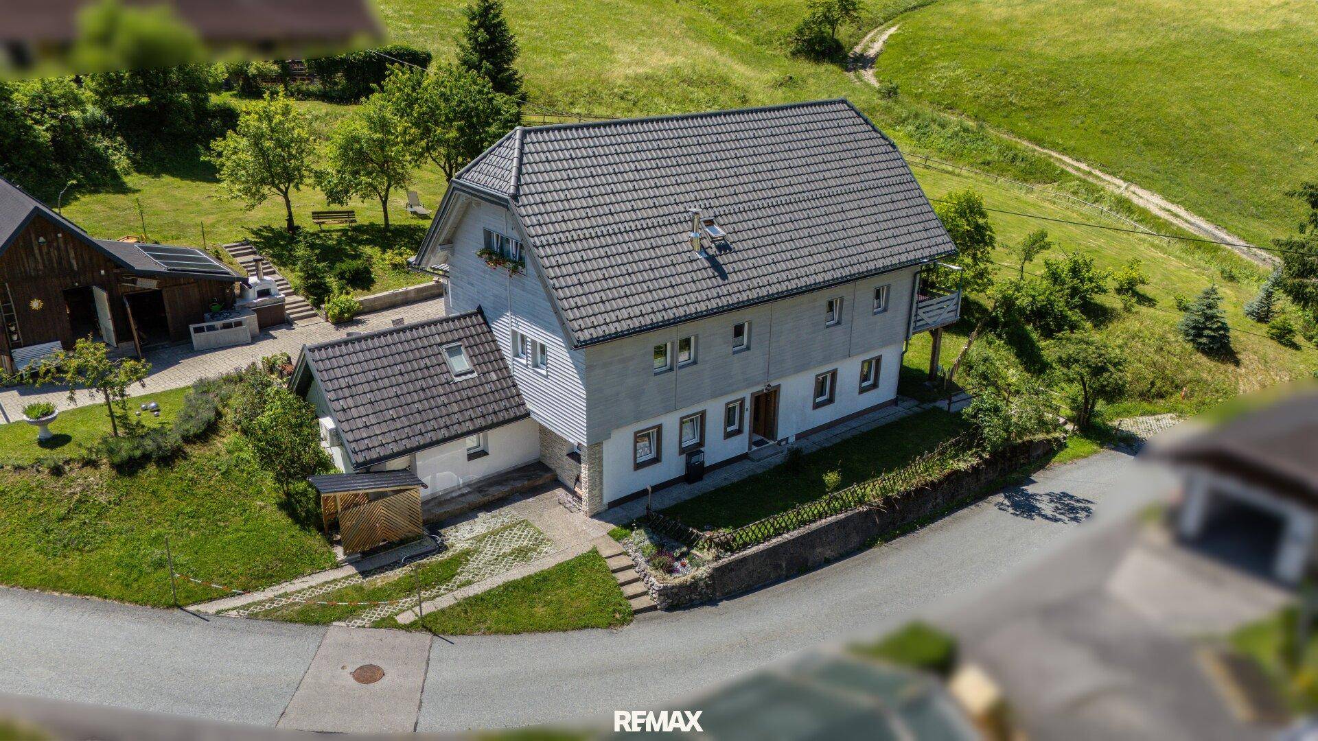 Luftaufnahme des Hauses mit Garten, Zufahrt und umliegender grüner Hügellandschaft.