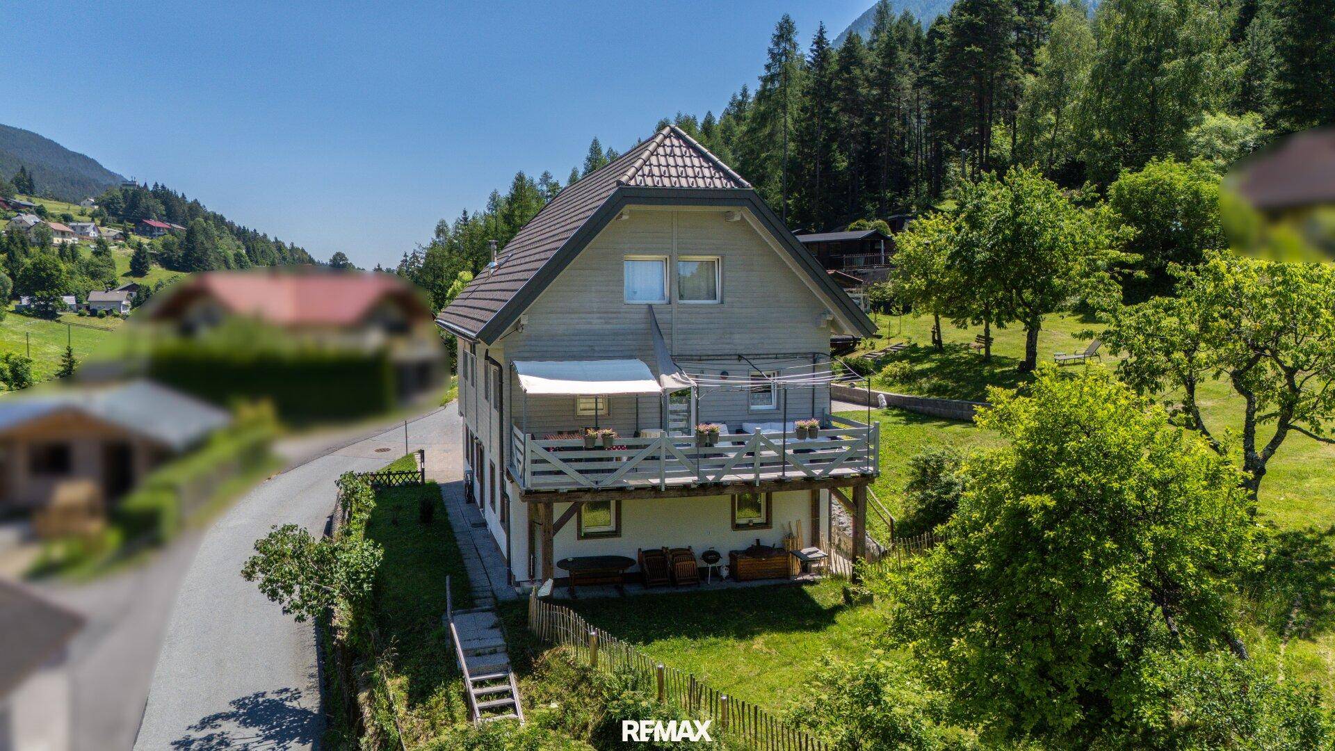 Seitenansicht des Hauses mit großem Balkon, Holzgeländer und Blick auf die bewaldeten Berge.