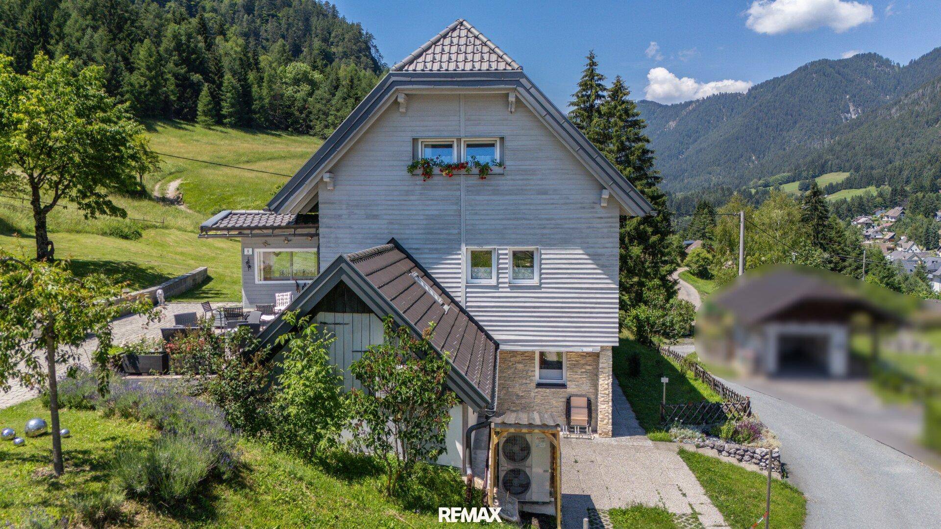 Hausfassade mit moderner Wärmepumpe, gepflegtem Gartenbereich und Bergblick im Hintergrund.