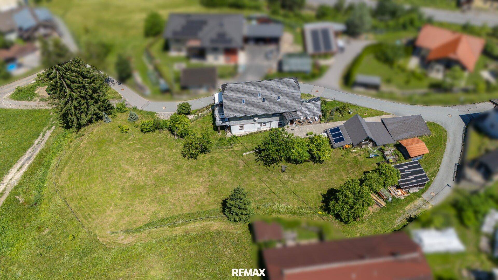 Luftaufnahme des Hauses mit weitläufigem Grundstück, umgeben von grünen Hügeln und Bäumen.