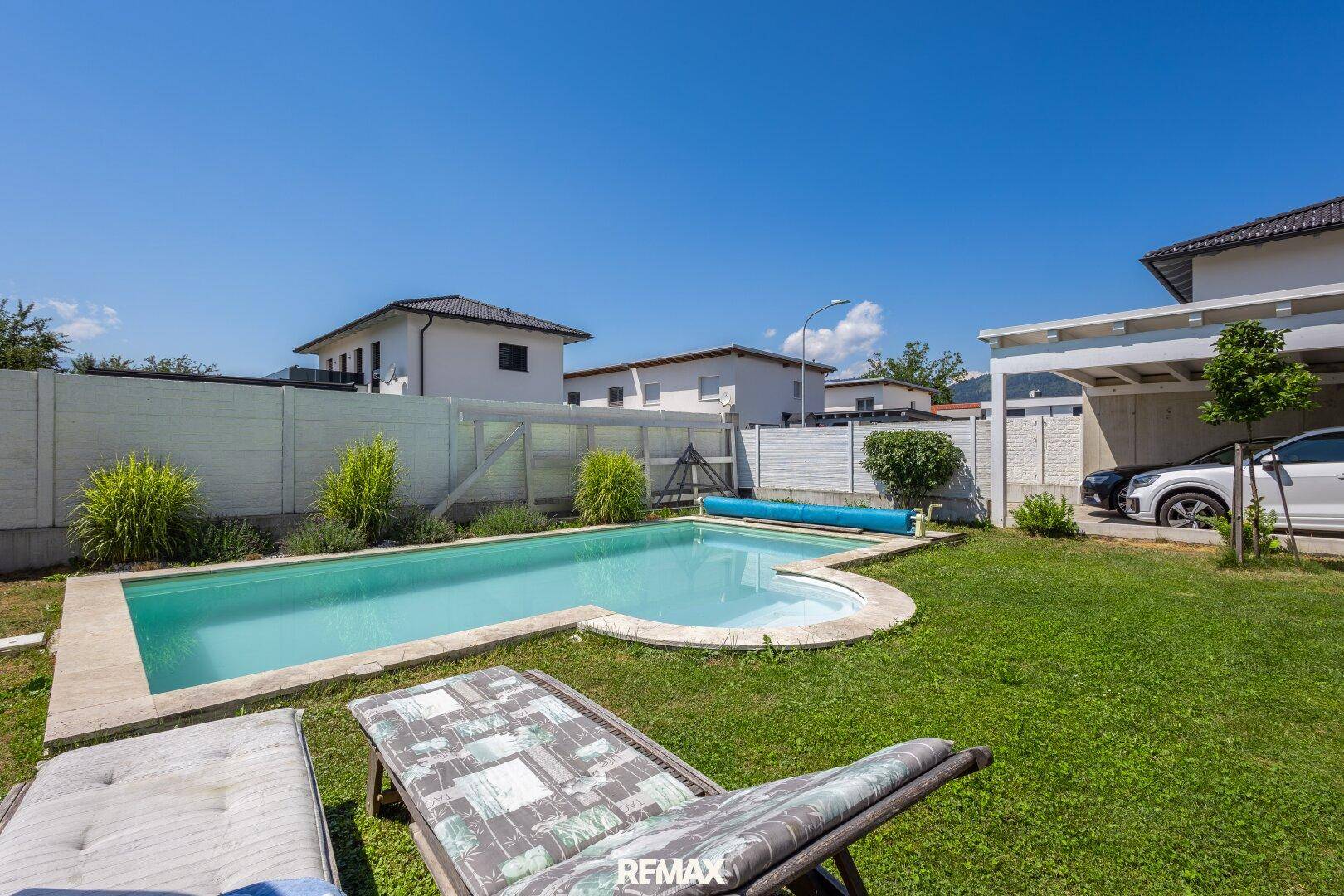 Gepflegter Garten mit Pool und Liegeflächen unter blauem Himmel.