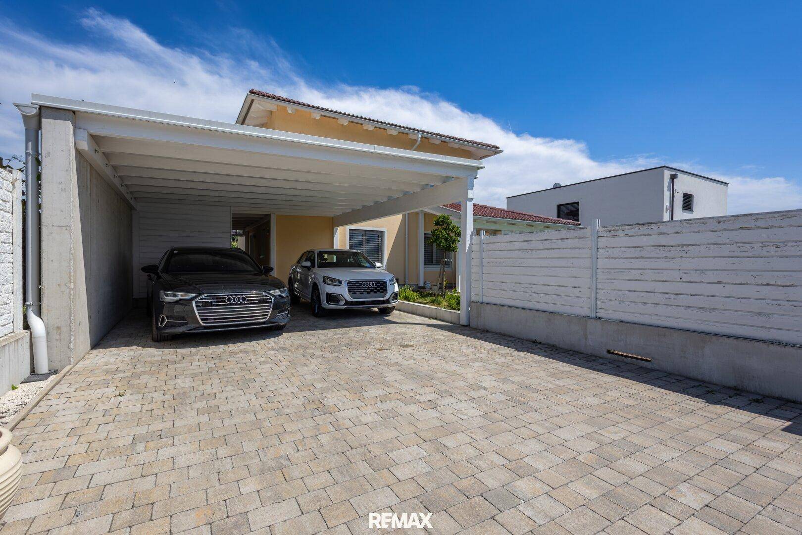 Überdachter Carport mit Stellplätzen für zwei Fahrzeuge und gepflasterter Einfahrt.