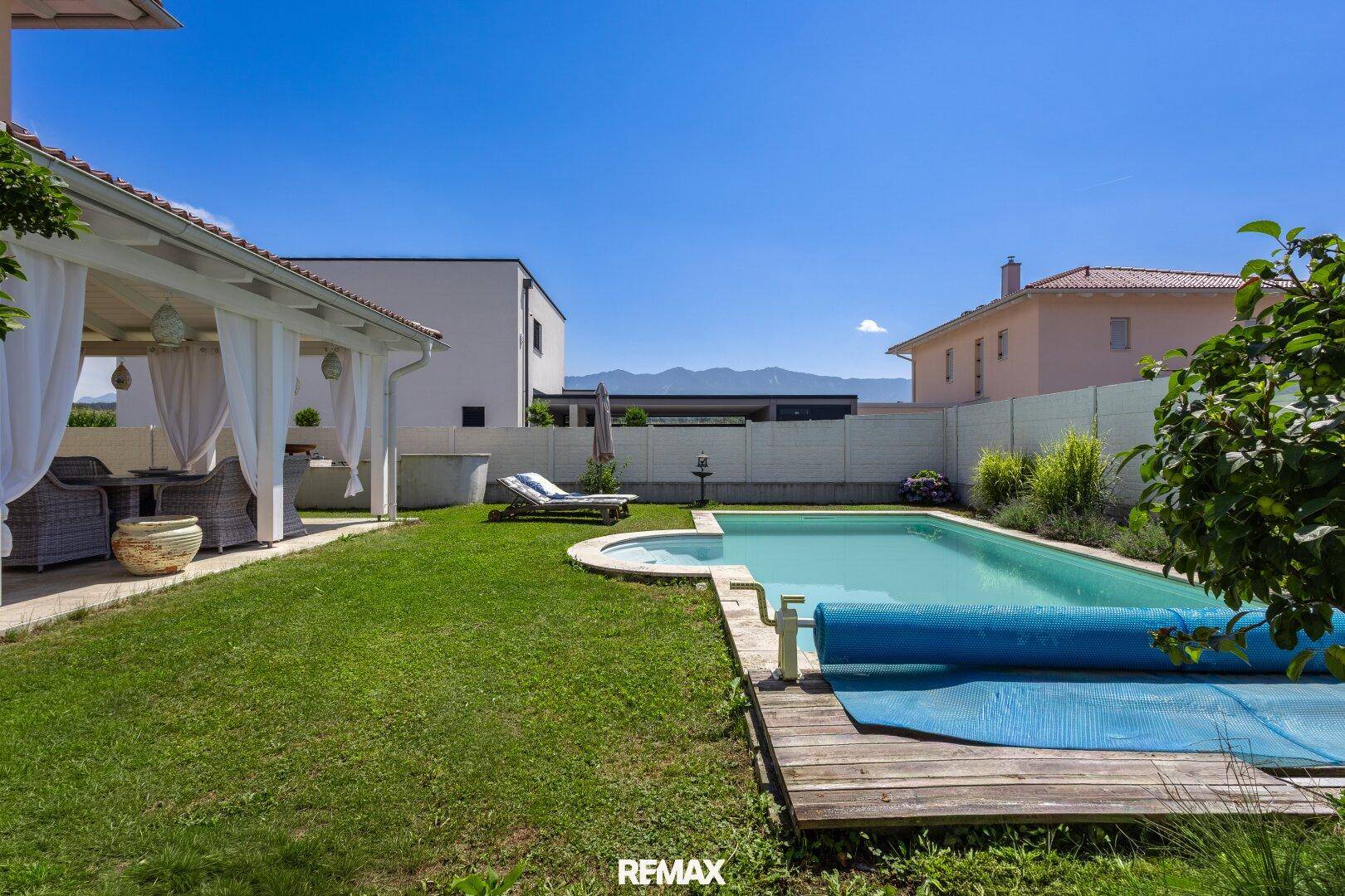 Sonniger Garten mit Swimmingpool, Liegestühlen und überdachtem Essbereich im Freien.